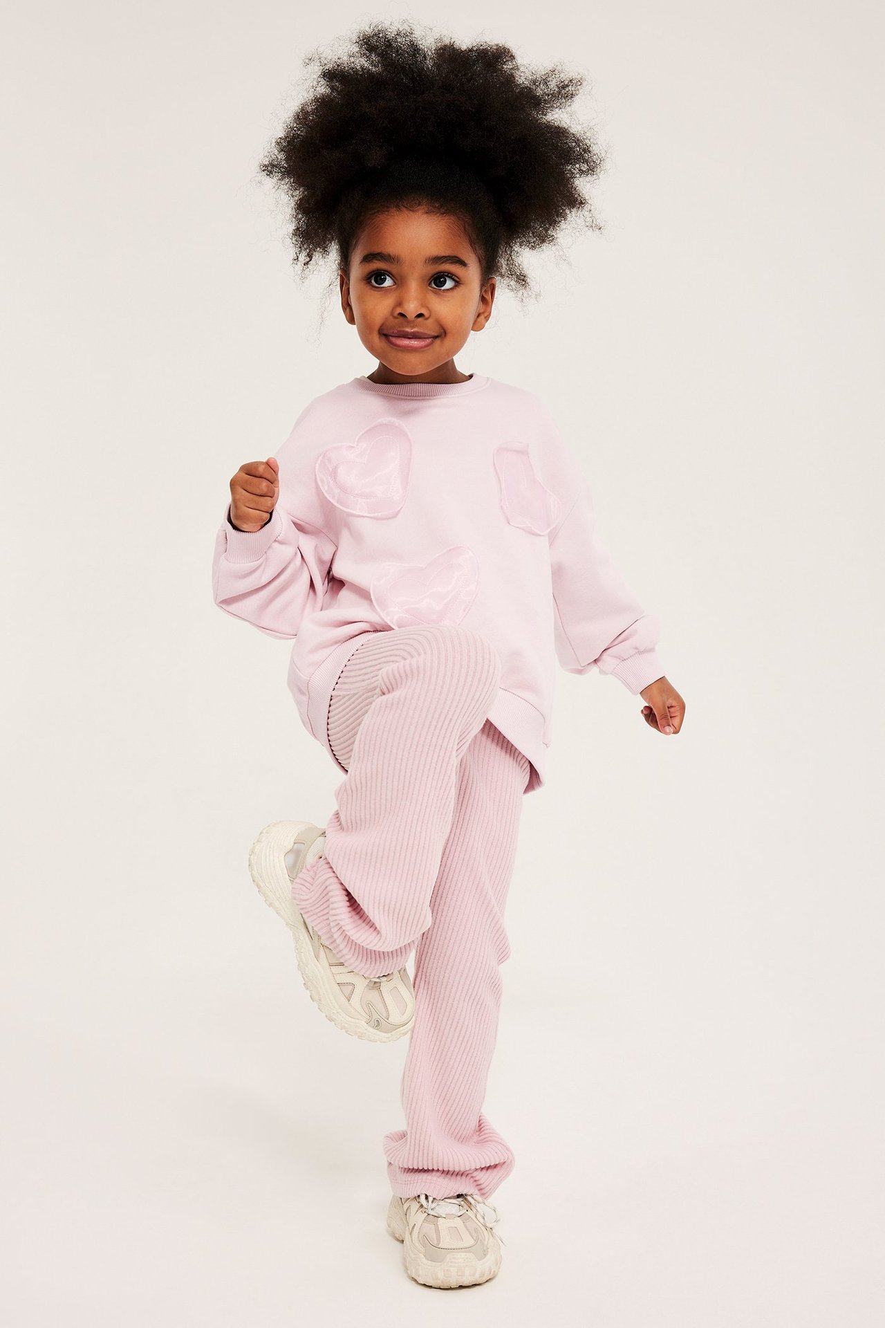 Dziecięca jasnoróżowa bluza z bawełny z aplikacjami serc z organzy, z ryflowanymi spodniami i sneakersami.