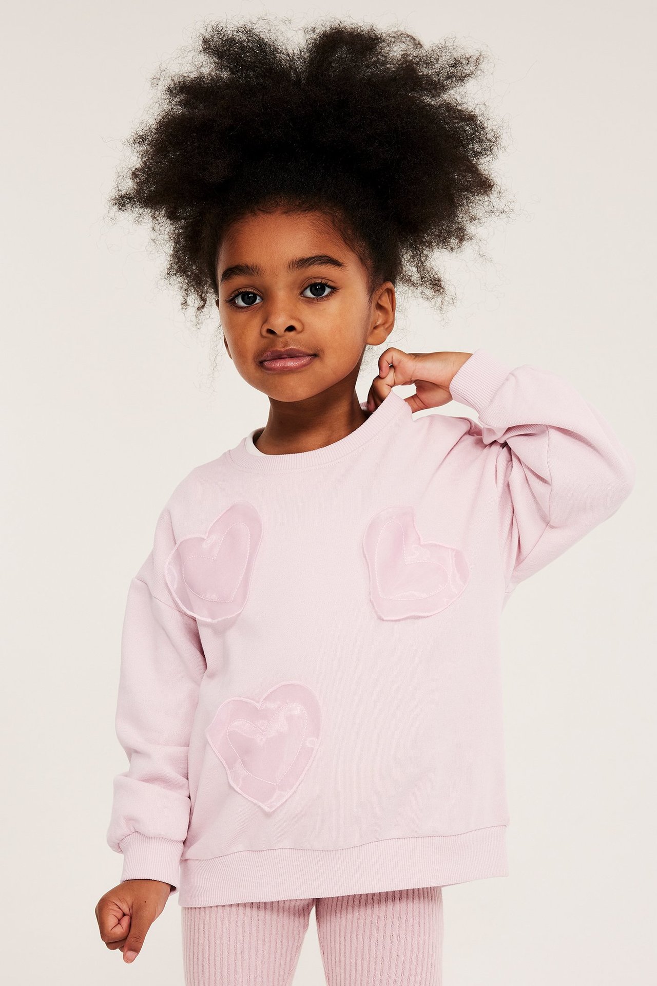 Widok z przodu dziecka w jasnoróżowej bluzie bawełnianej z sercami z organzy i pasujących legginsach.