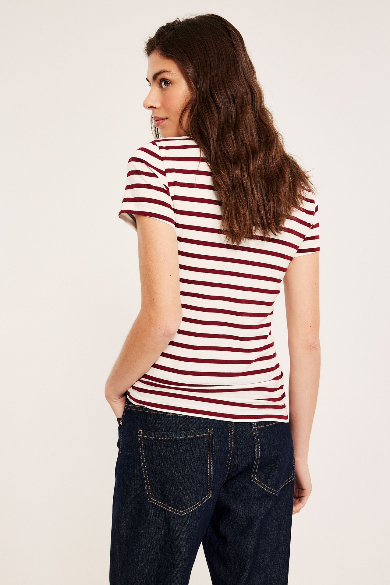 Siden bakfra av kvinne i en tettsittende hvit- og mørkerød stripet kortermet topp og mørkeblå jeans.