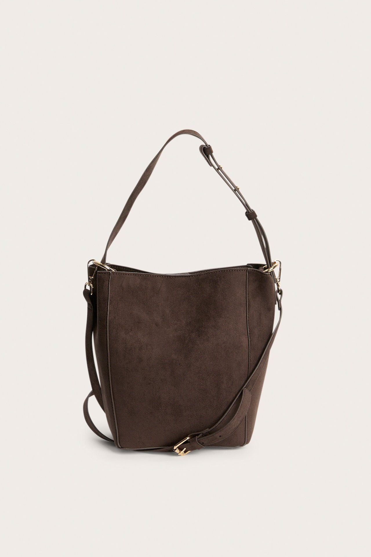 Frontvisning av en mørkebrun bøtteveske i imitert semsket skinn med justerbar reim og gullspenne.