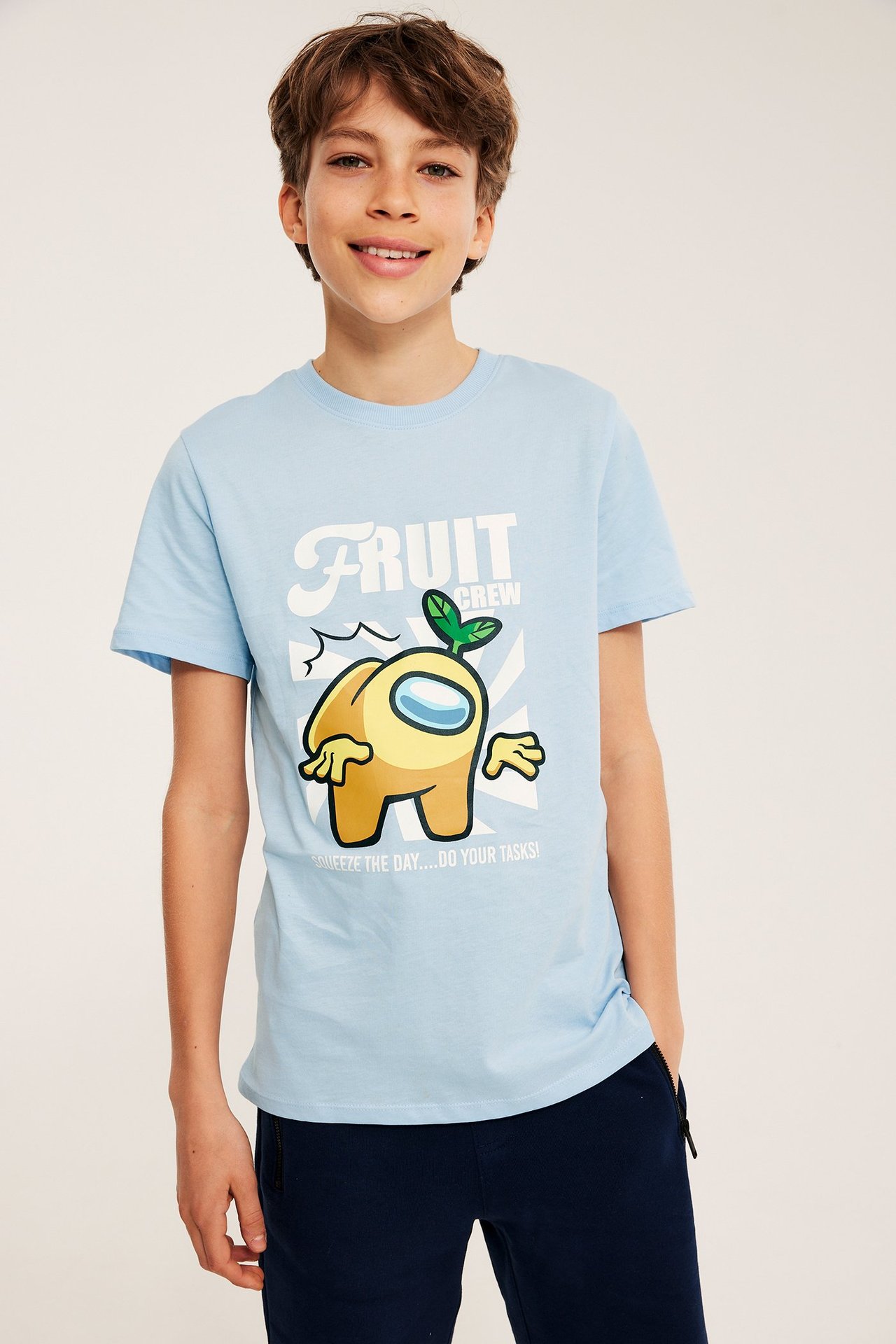 Edestä: Poika vaaleansinisessä Among Us "Fruit Crew" -T-paidassa ja tummansinisissä shortseissa.