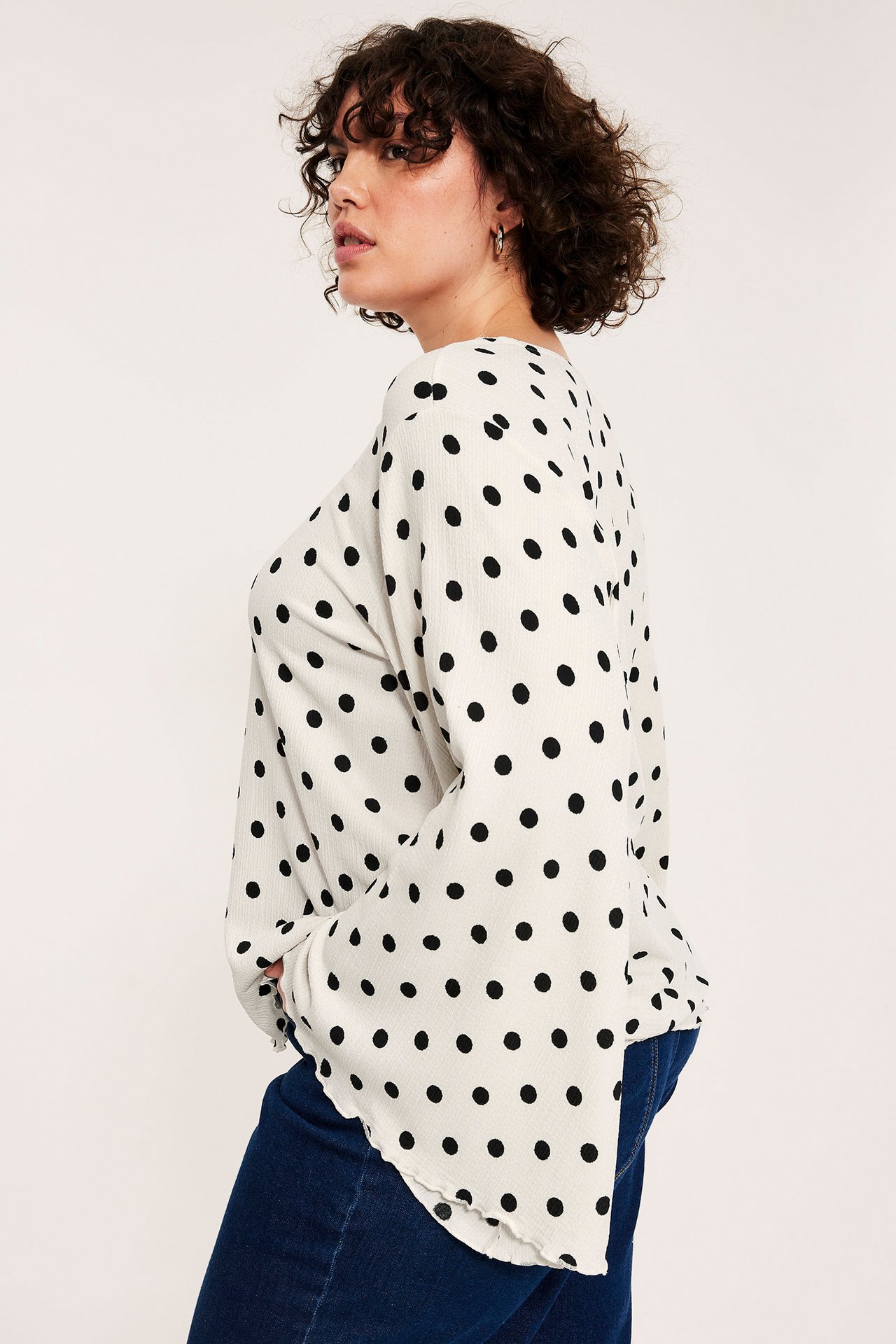 Sidovy av en kvinna i en offwhite prickig blus med vida ärmar, stylad med mörkblå jeans.