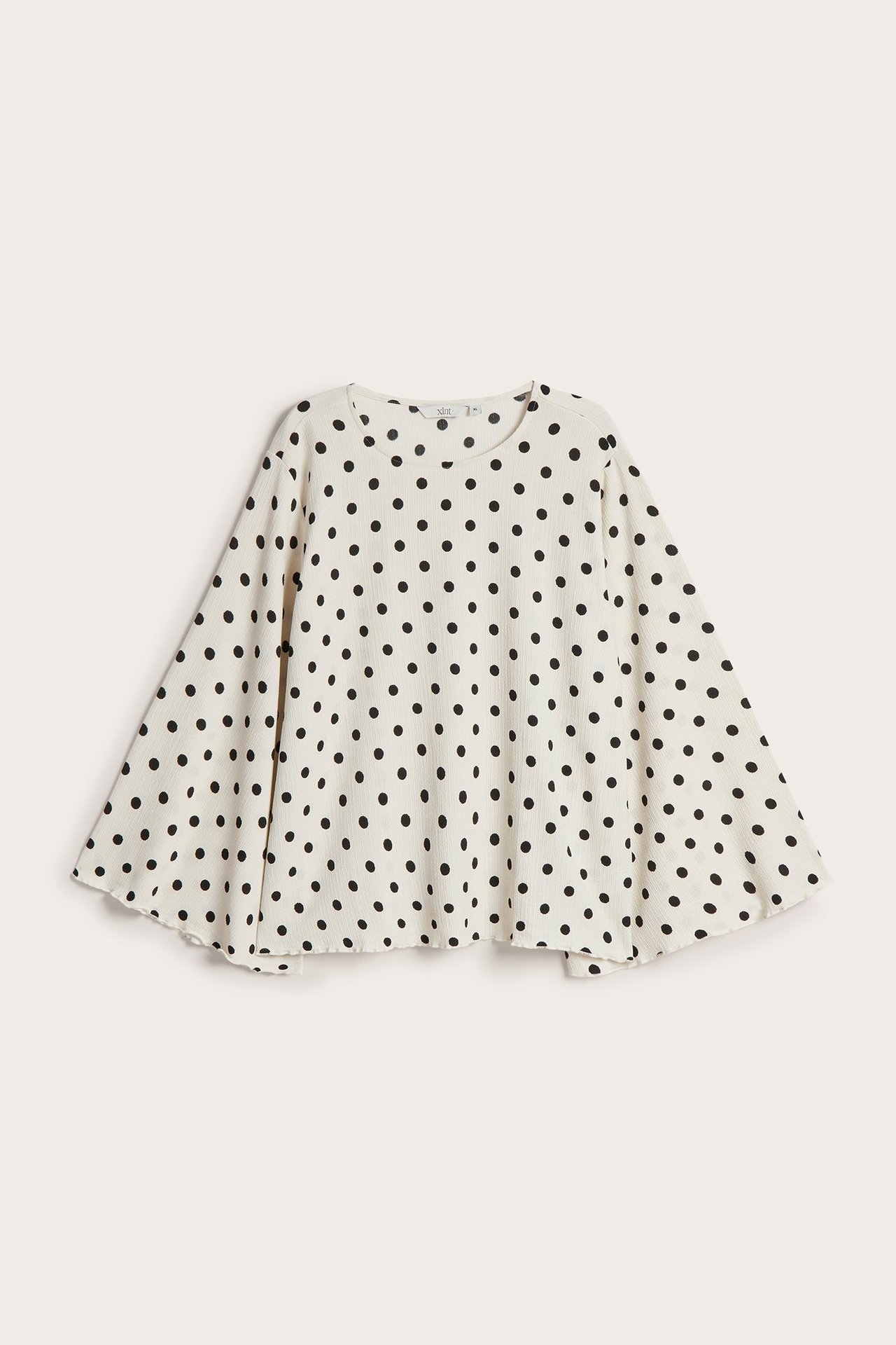 Forfra: Offwhite polyesterbluse med sorte prikker og vide, flagrende ermer.