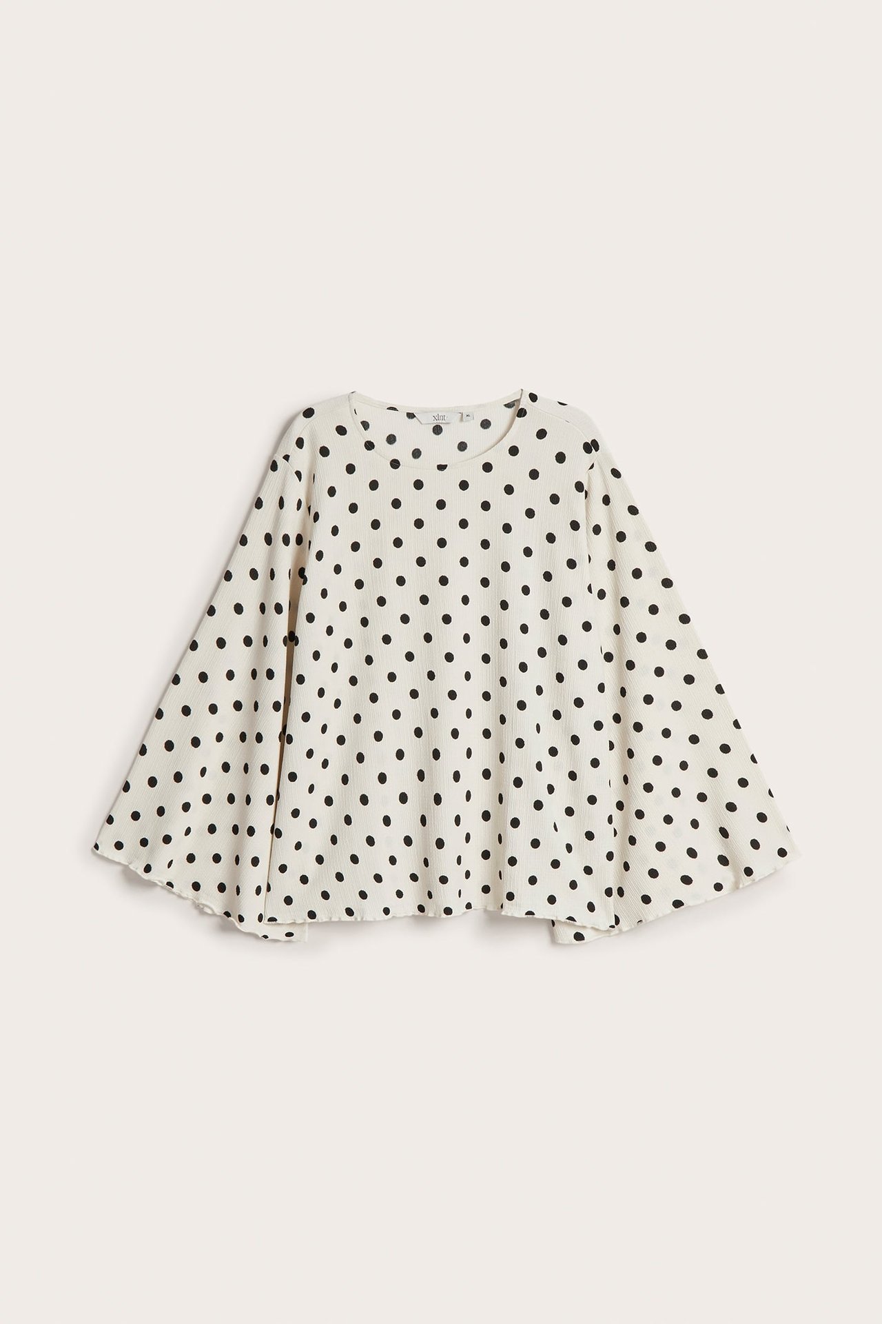 Forfra, løs off-white bluse med svarte prikker og utsvingte ermer.