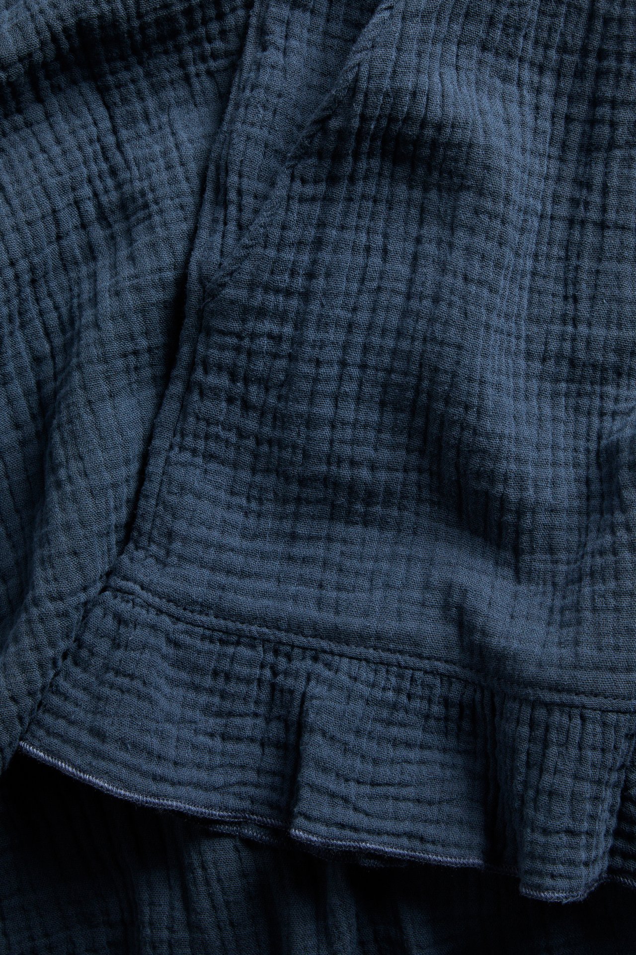 Närbild av mörkblå pyjamasshorts i muslin med en subtil volangdetalj vid benslutet.