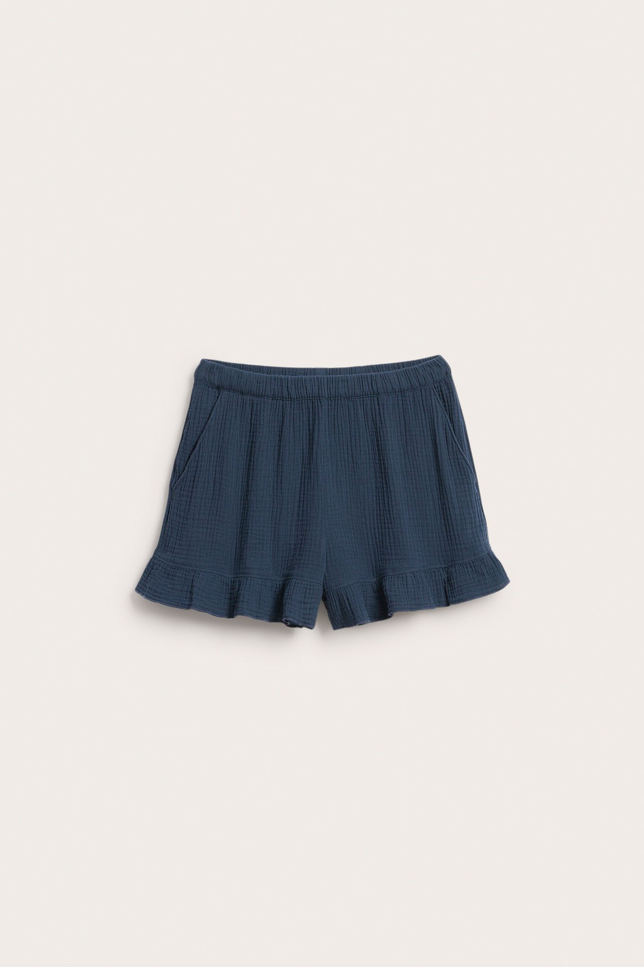 Framifrån: Mörkblå pyjamasshorts i muslin med resår i midjan, sidfickor och volang i benslut.