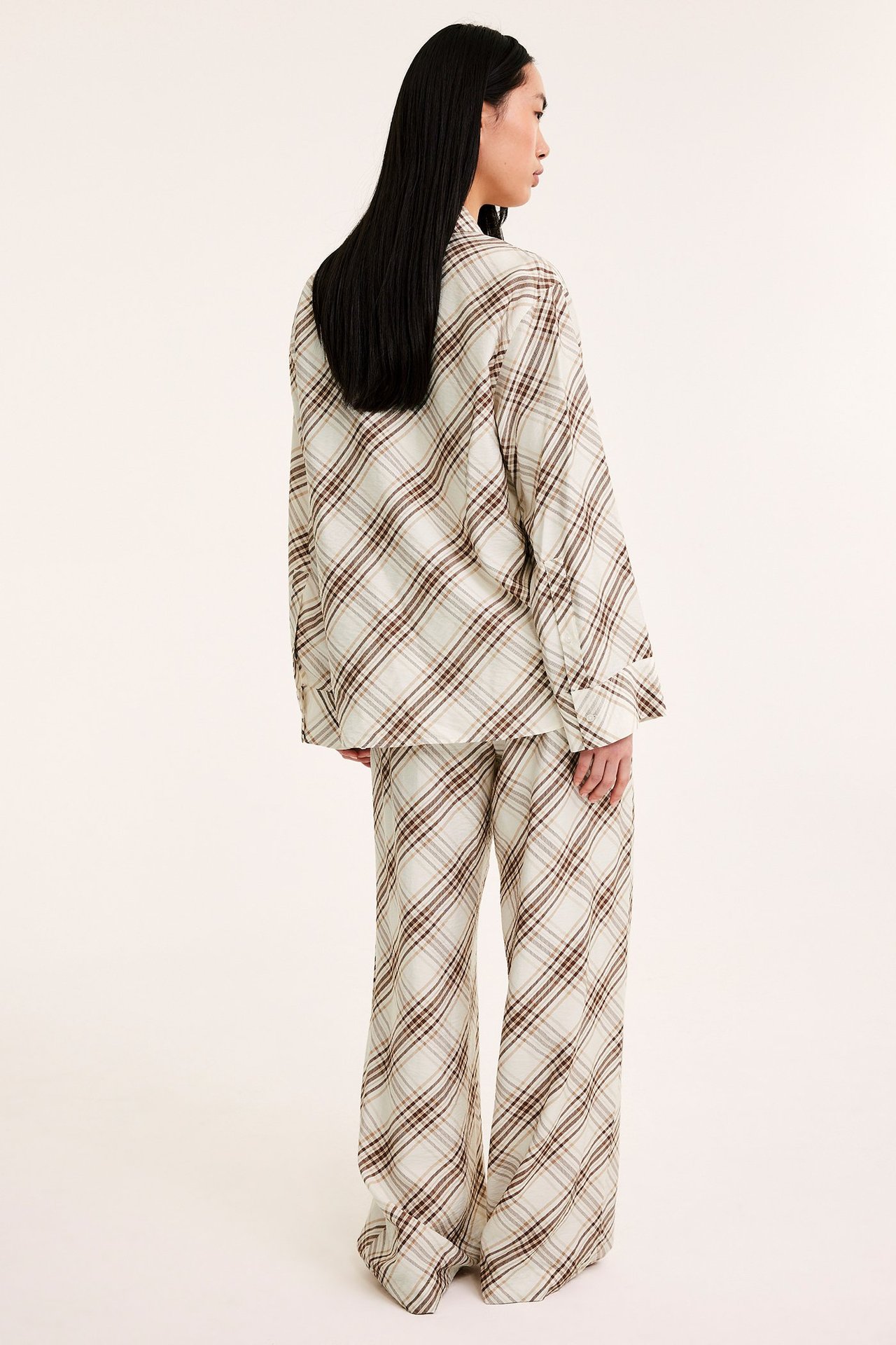 Widok z tyłu kobiety w beżowych, szerokich, wzorzystych spodniach wiskozowych i pasującej koszuli z długim rękawem.