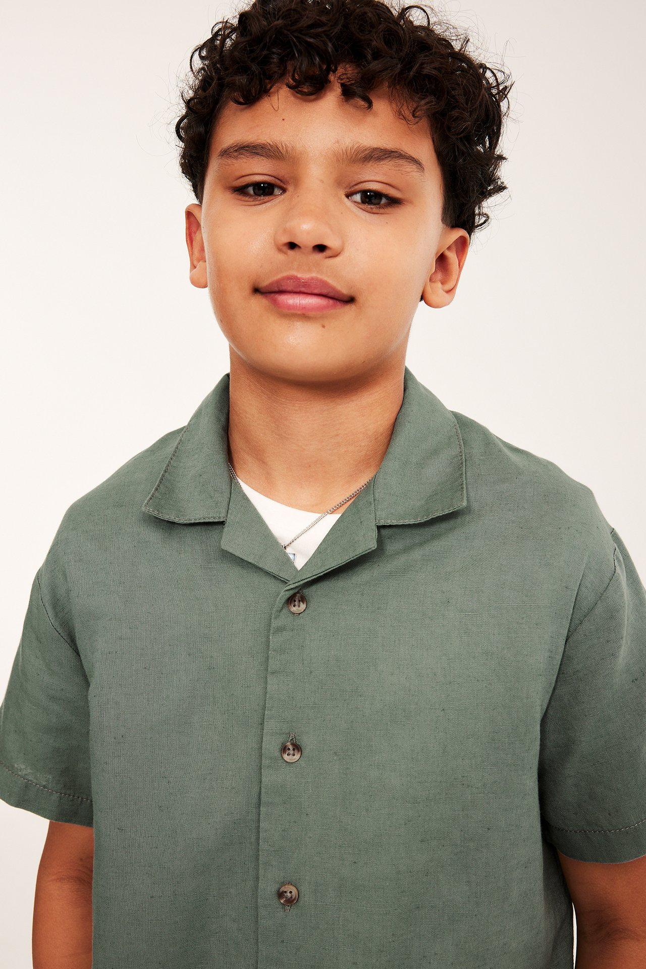 Lähikuva edestä lapsesta yllään tummanvihreä lyhythihainen pellavasekoitespaita valkoisen t-paidan päällä.