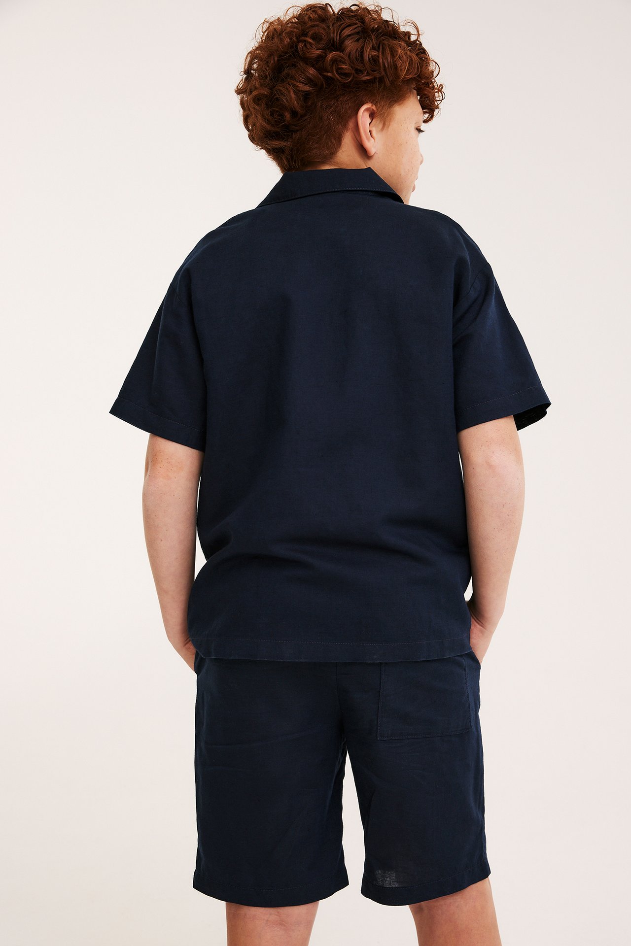Widok z tyłu dziecka w granatowej koszuli z krótkim rękawem z lnu i pasujących szortach.
