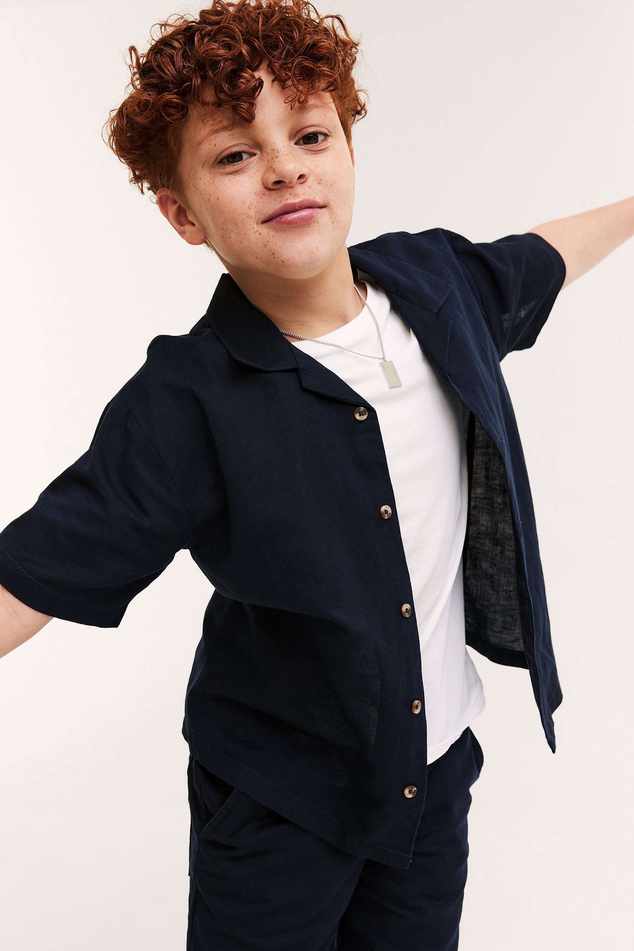 Lapsi yllään tummansininen lyhythihainen pellavapaita, valkoinen t-paita, tummat shortsit ja hopeakaulakoru.