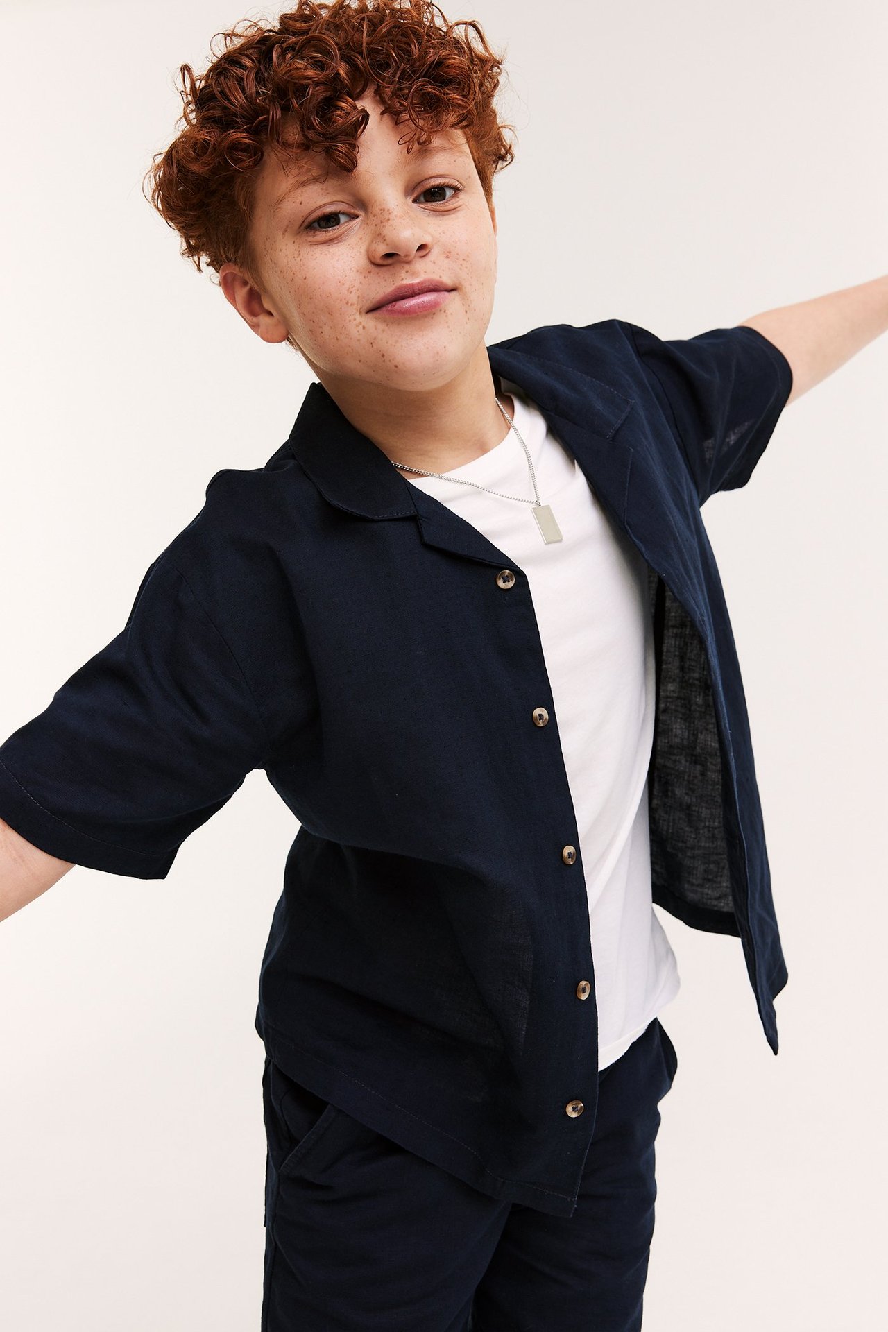 Lapsi yllään tummansininen lyhythihainen pellavapaita, valkoinen t-paita, tummat shortsit ja hopeakaulakoru.