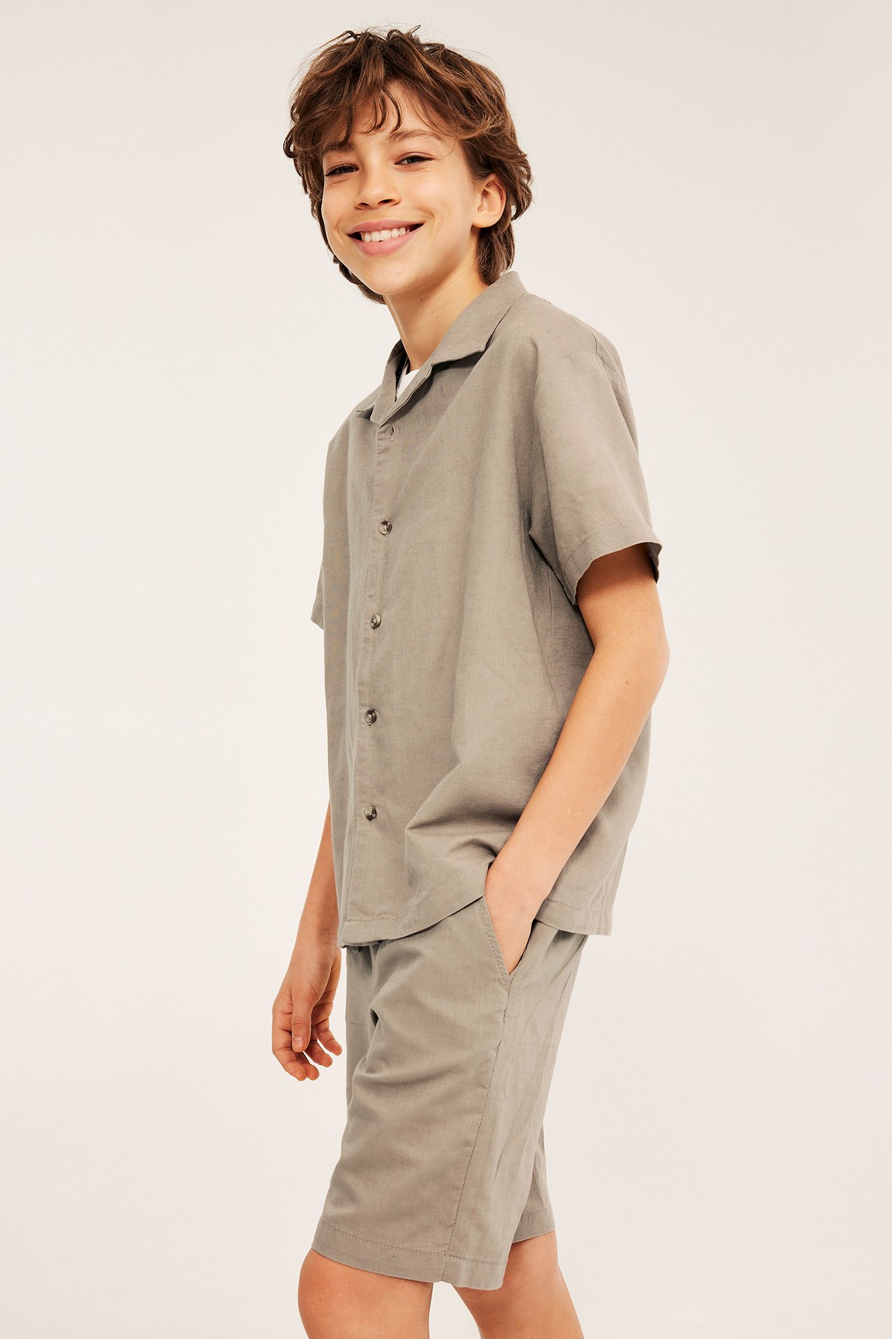 Sivukuva hymyilevästä lapsesta yllään beigen lyhythihainen pellavasekoitepaita ja yhteensopivat shortsit.