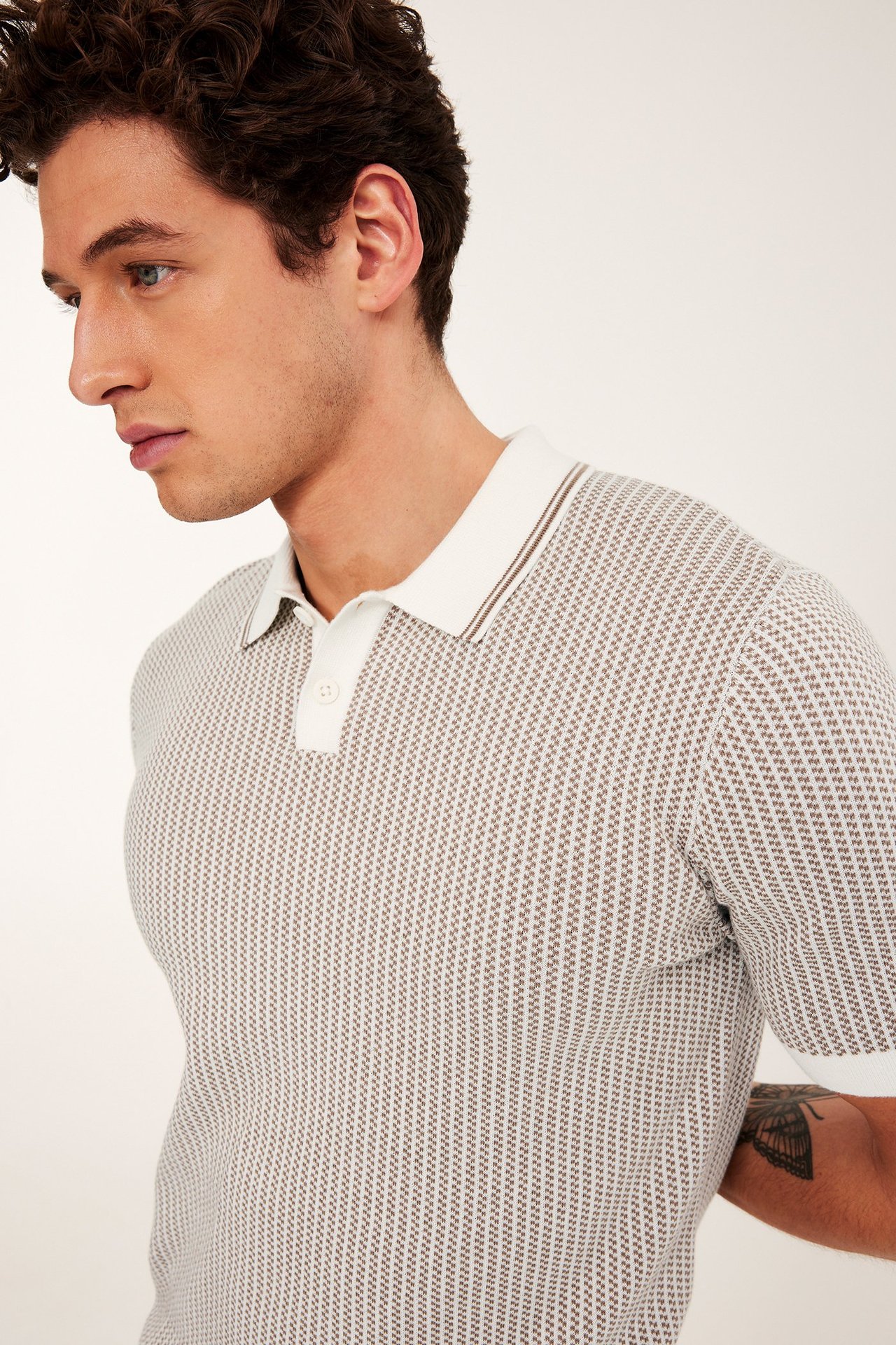 Mann med beige jacquardstrikket pikéskjorte med korte ermer, hvit krage og to knapper.