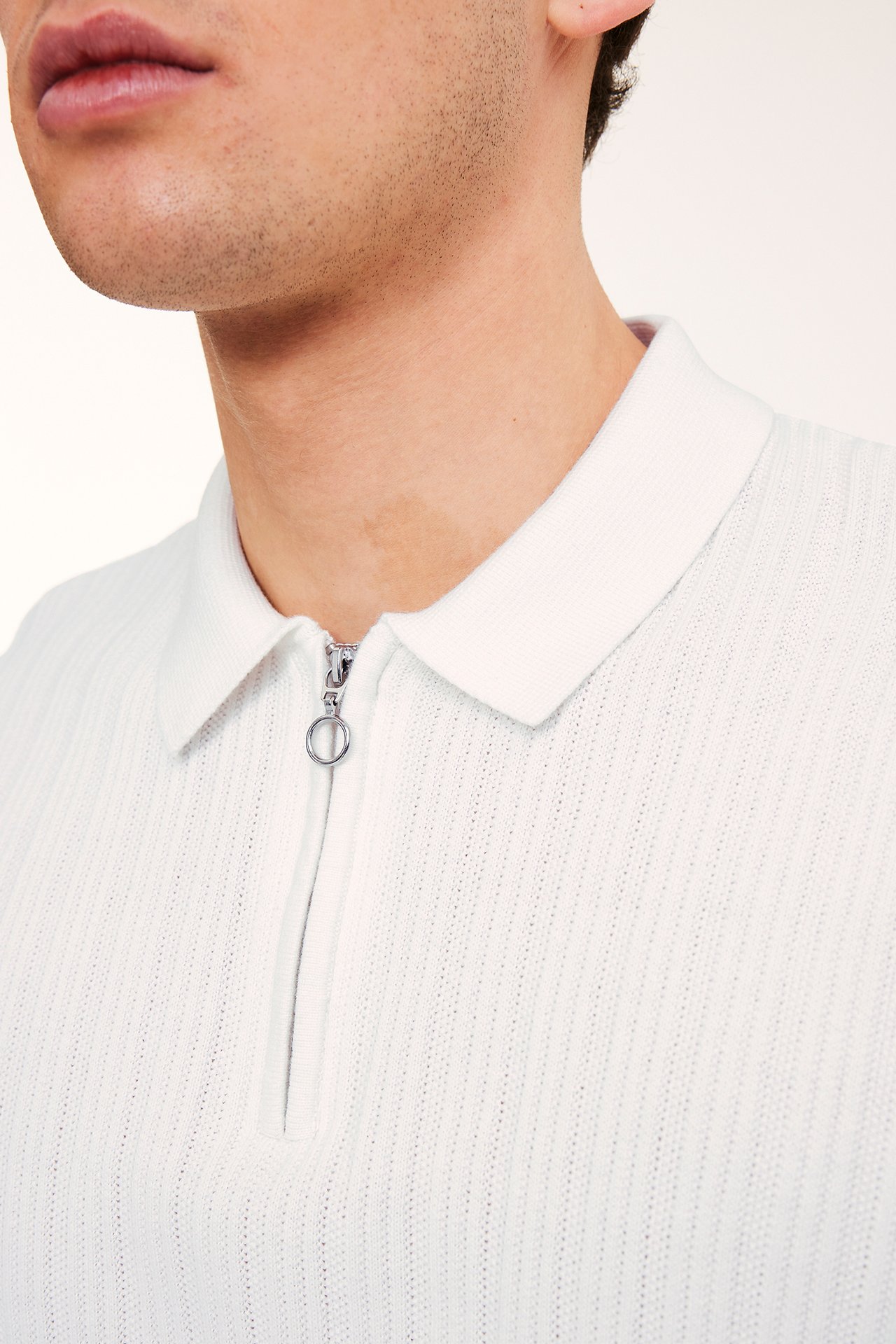 Zbliżenie mężczyzny w ecru, dzianinowej koszulce polo z kołnierzykiem, zamkiem i strukturalnym wzorem.