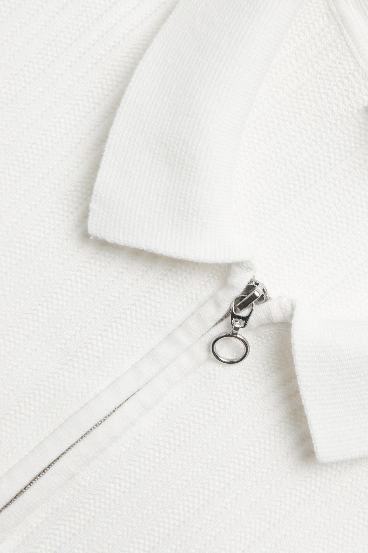 Zbliżenie na kremową dzianinową koszulkę polo z kołnierzykiem, fakturą i zamkiem błyskawicznym.