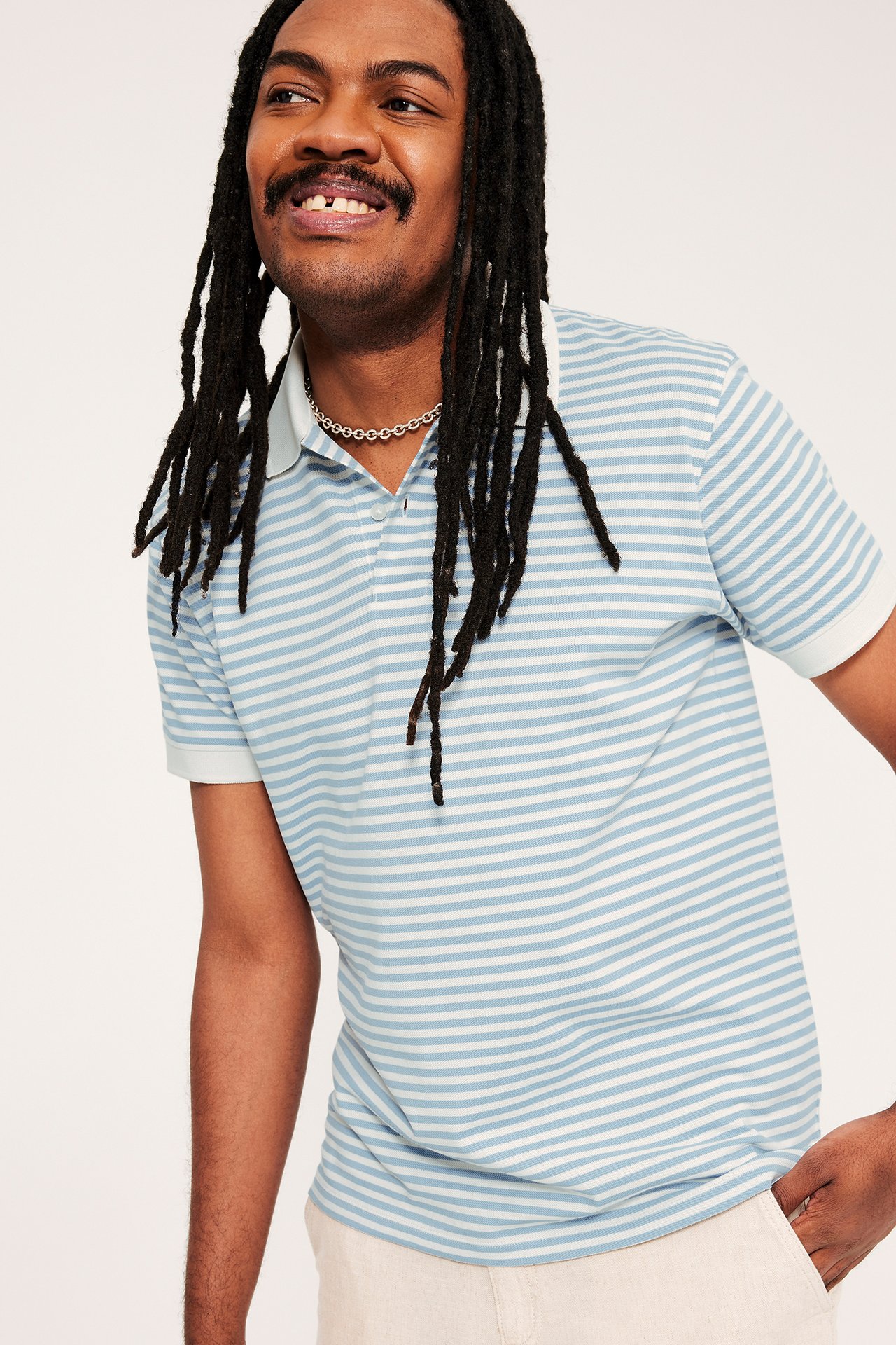 Mies yllään vaaleansinivalkoinen raidallinen puuvillapikeepaita kauluksella ja kahdella napilla.