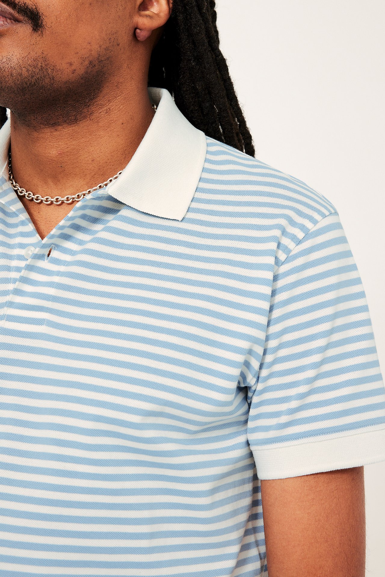 Lähikuva, edestä: Mies sinivalkoraidallisessa pikeepaidassa, jossa valkoinen kaulus ja hopeaketju.