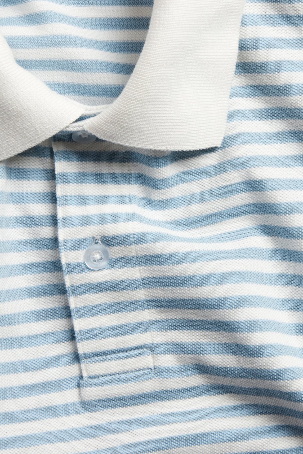 Närbild av en blåvitrandig pikétröja i bomullspiké med vit krage och knappslå.