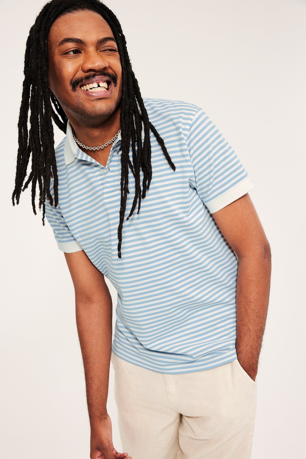 Sinisävyinen raidallinen pikeepaita kauluksella, kahdella napilla, miehellä beigeissä housuissa.