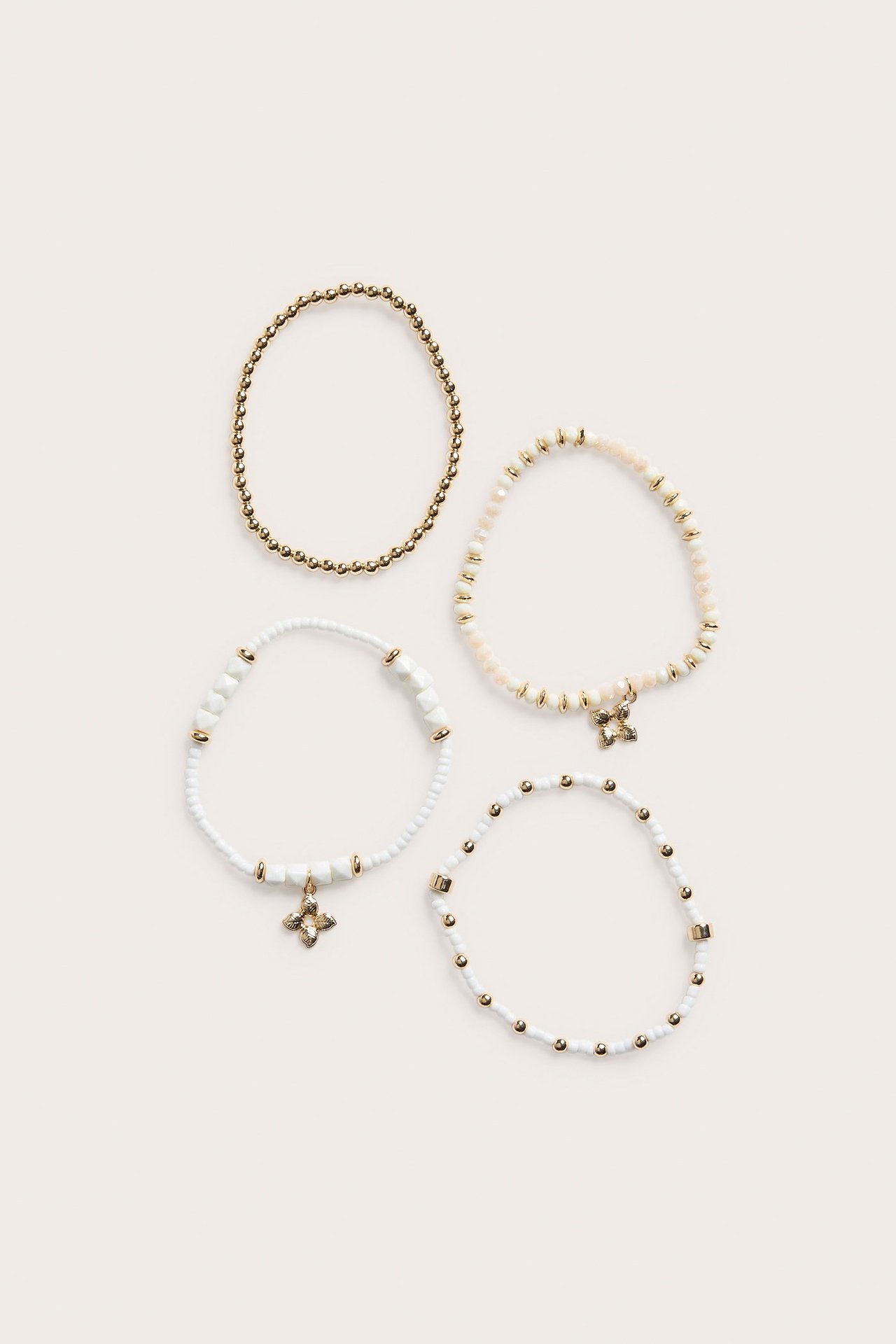 Uppifrån, ett 4-pack elastiska pärlarmband i vitt och guld, två med berlocker.
