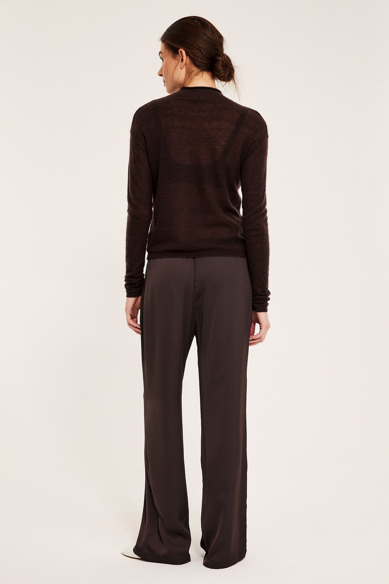 Kvinne bakfra i mørkebrune vide satengbukser og mørkebrun gjennomsiktig langermet topp.