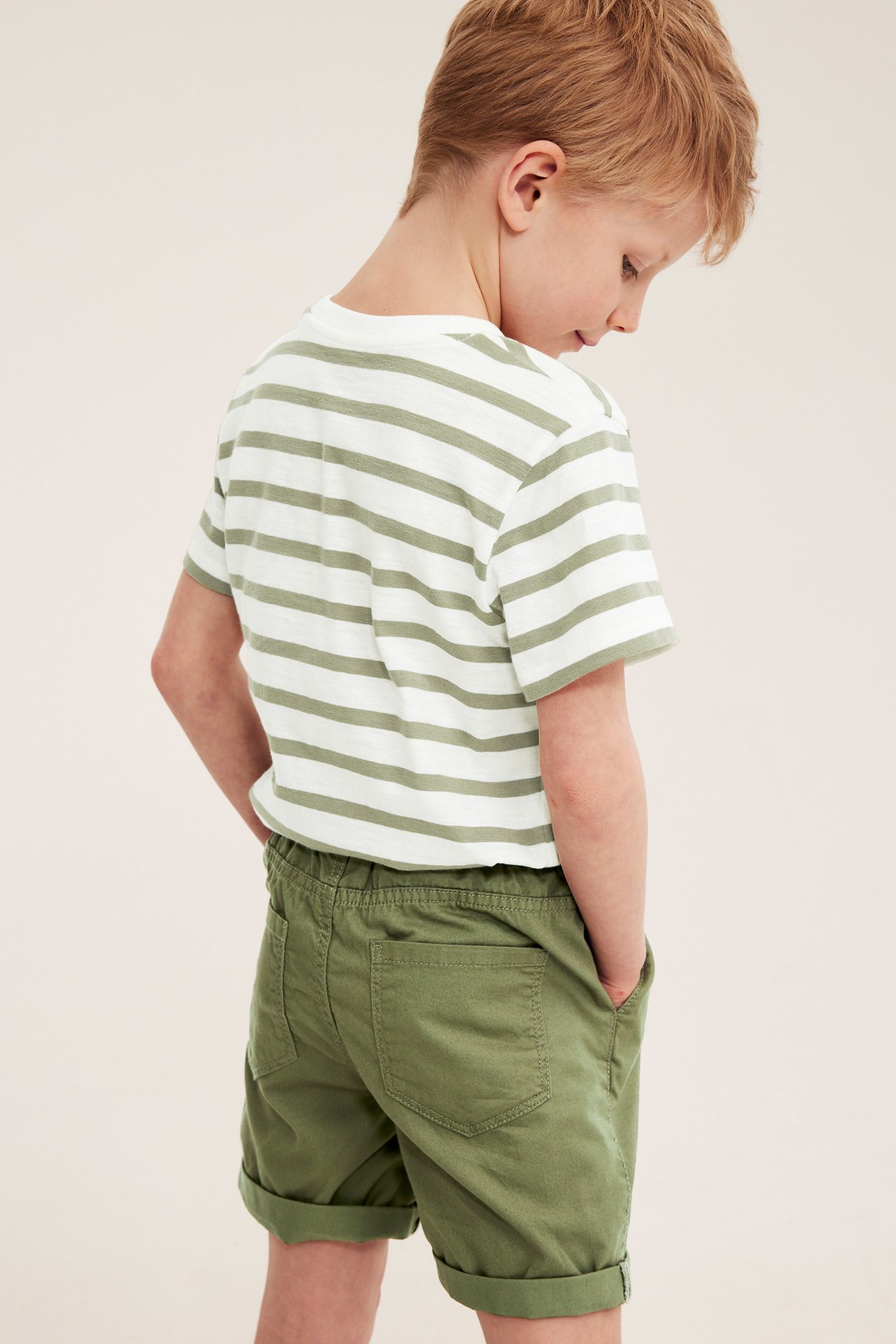 Dziecko z tyłu w ciemnozielonych bawełnianych szortach z podwiniętymi nogawkami i w pasiastym podkoszulku.