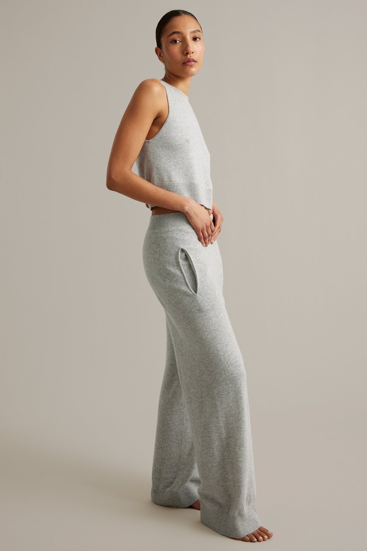 Sivukuva: Nainen yllään vaaleanharmaat villakashmir-leveälahkeiset housut taskuilla ja hihaton toppi.