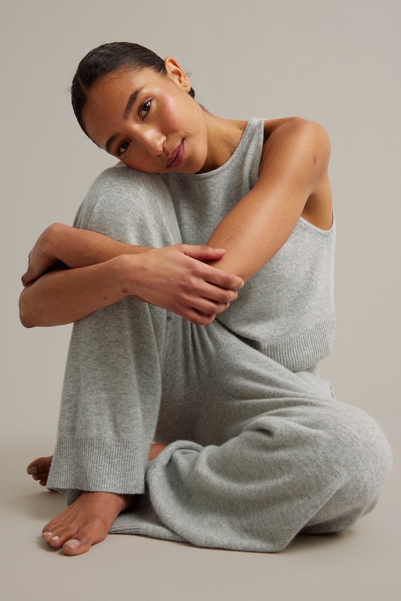 Edestäpäin: Nainen istuu vaaleanharmaissa neulotuissa leveälahkeisissa housuissa ja yhteensopivassa topissa.