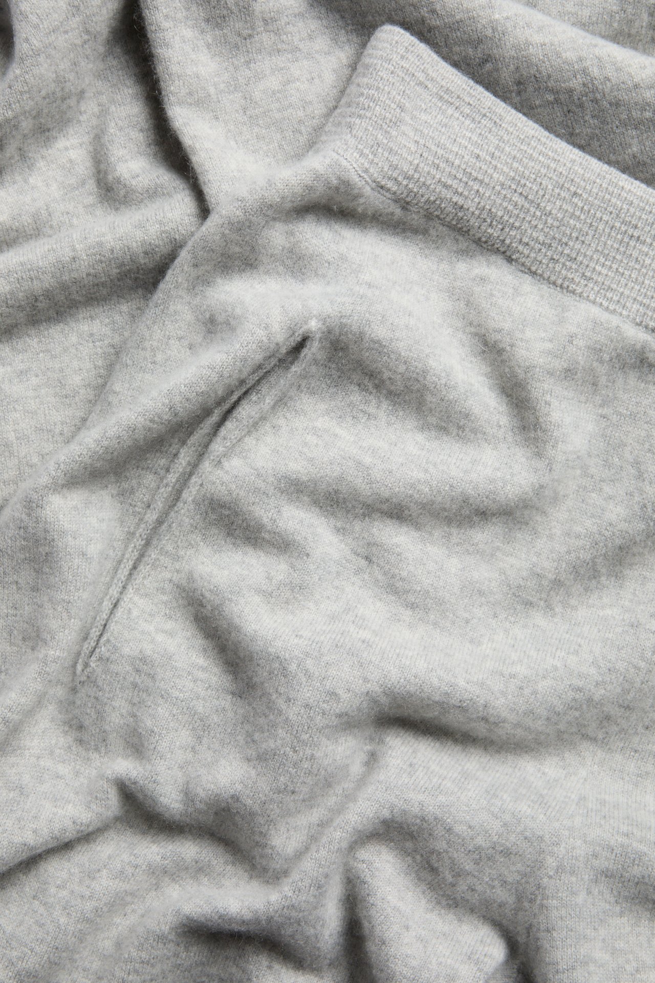Närbild av ljusgrå melerade stickade byxor i ull/kashmirblandning, med sidoficka och ribbad kant.