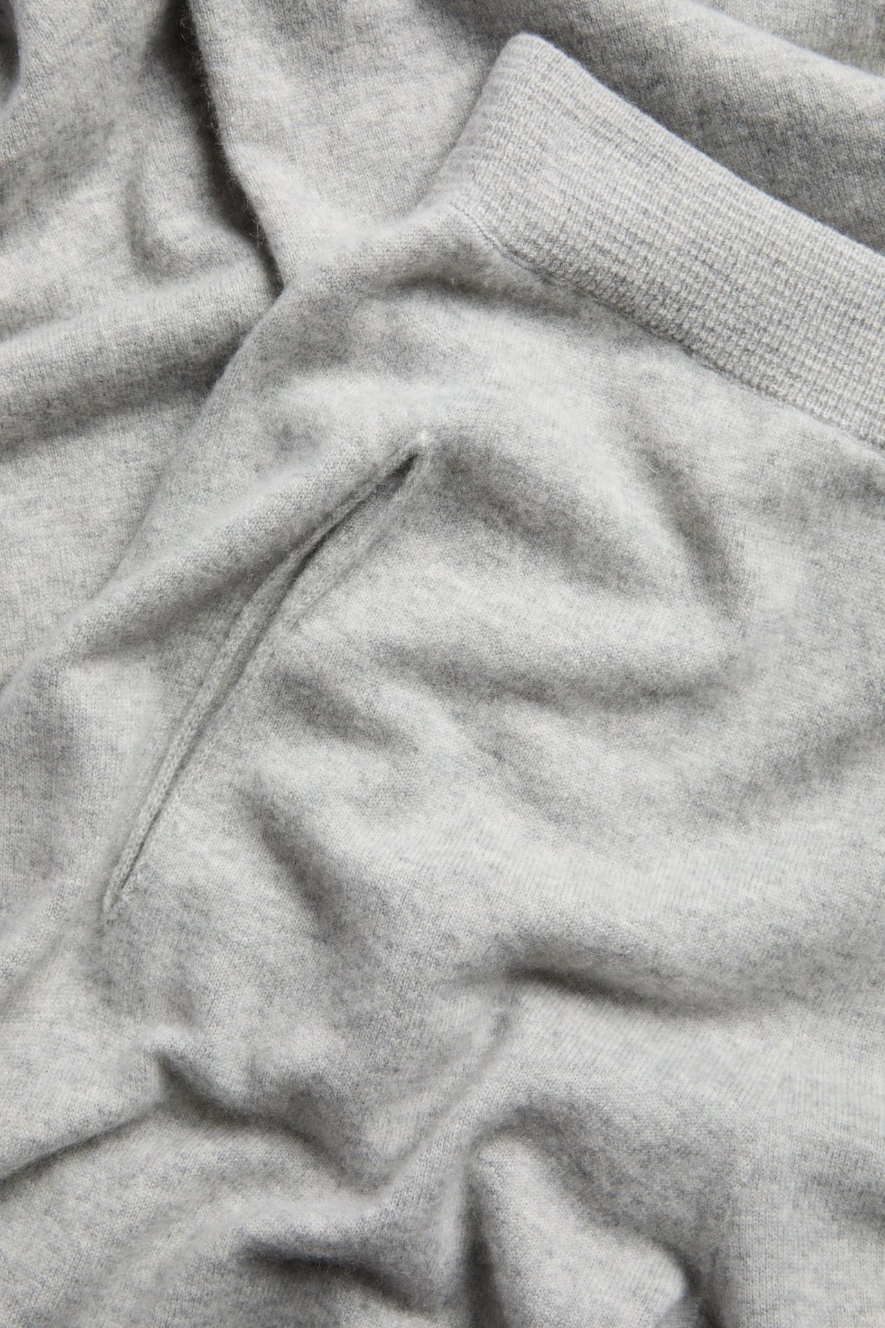 Närbild av ljusgrå melerade stickade byxor i ull/kashmirblandning, med sidoficka och ribbad kant.