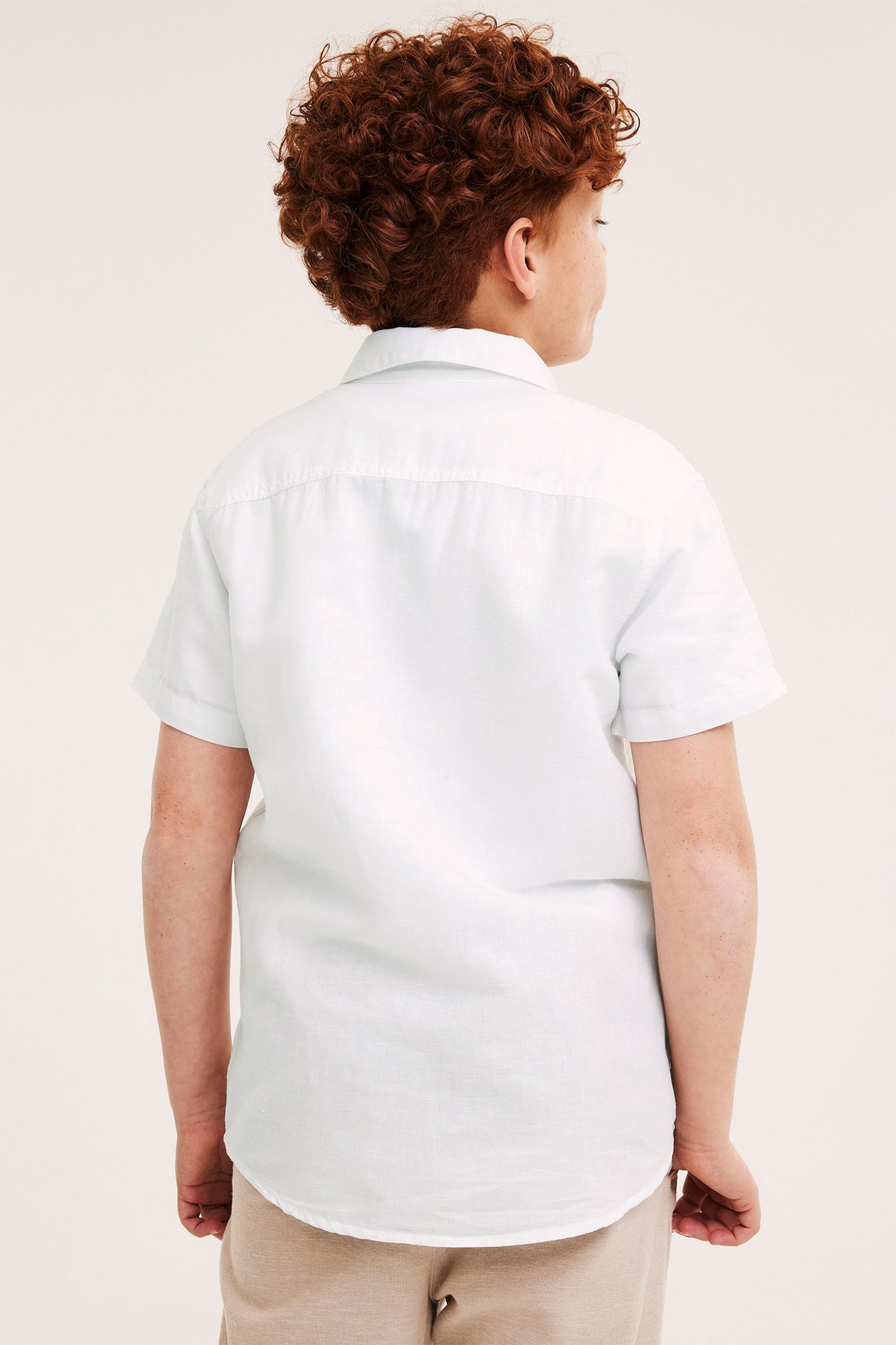 Ryggbilde av et barn med hvit kortermet linskjorte og beige shorts.