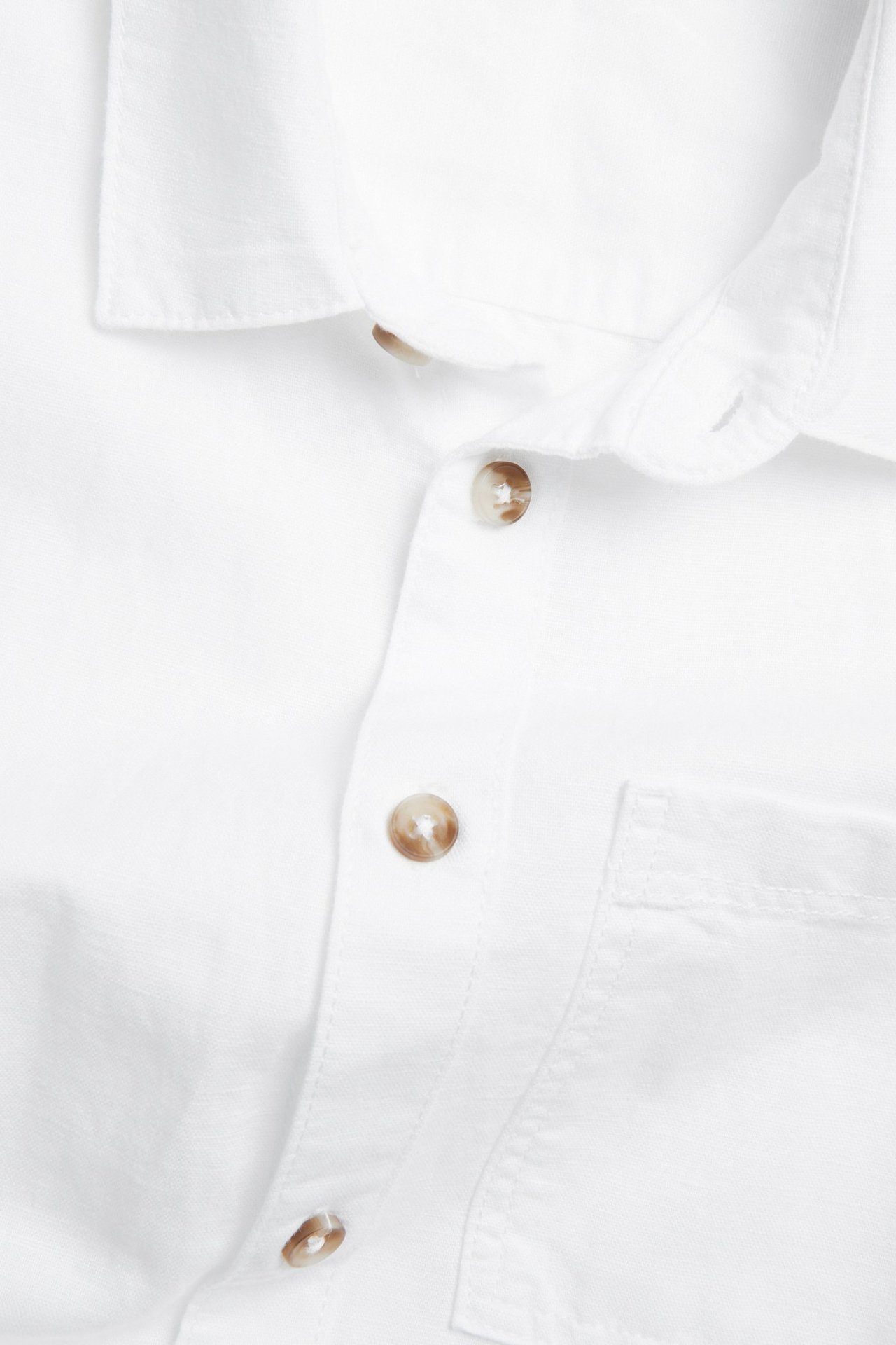 Närbild på en vit skjorta i linnemix med bruna knappar på knäppningen och en bröstficka.