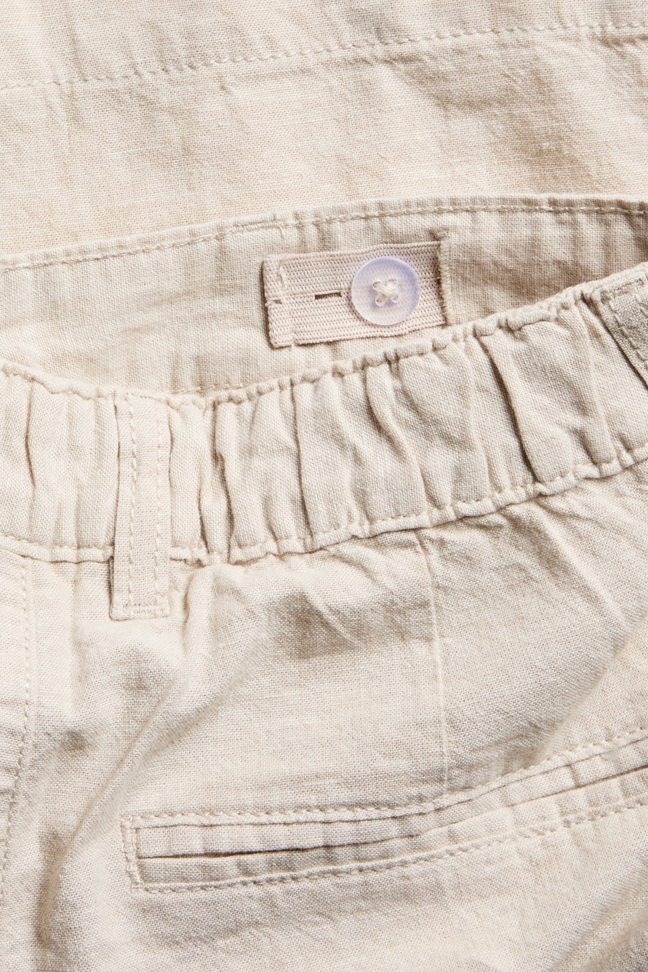 Lähikuva vaaleanbeigestä pellavasekoiteshortseista, joissa resori vyötärö ja säädettävä nappi.