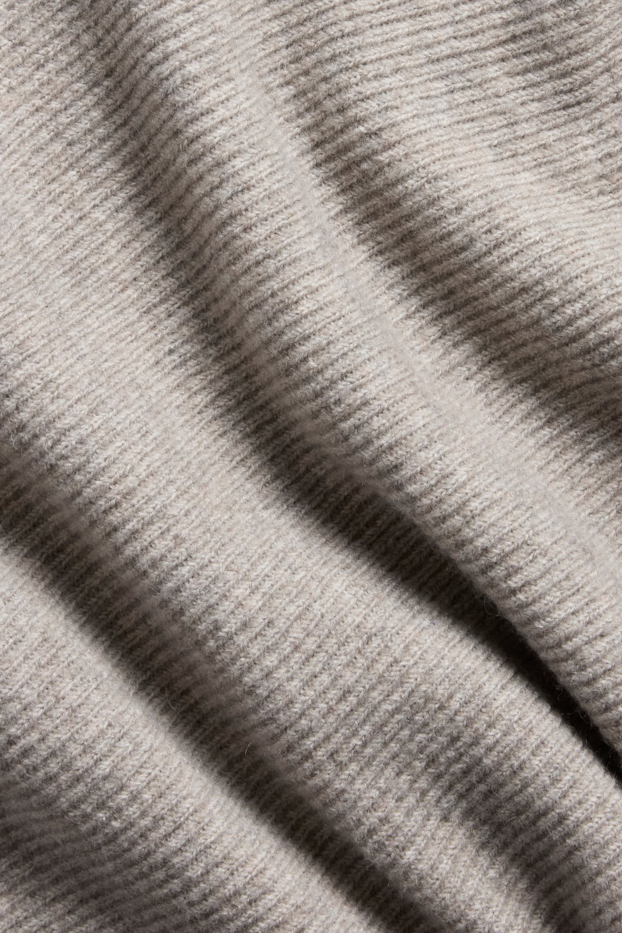 Närbild av ett beigemelange stickat tyg med en subtil ribbad struktur.