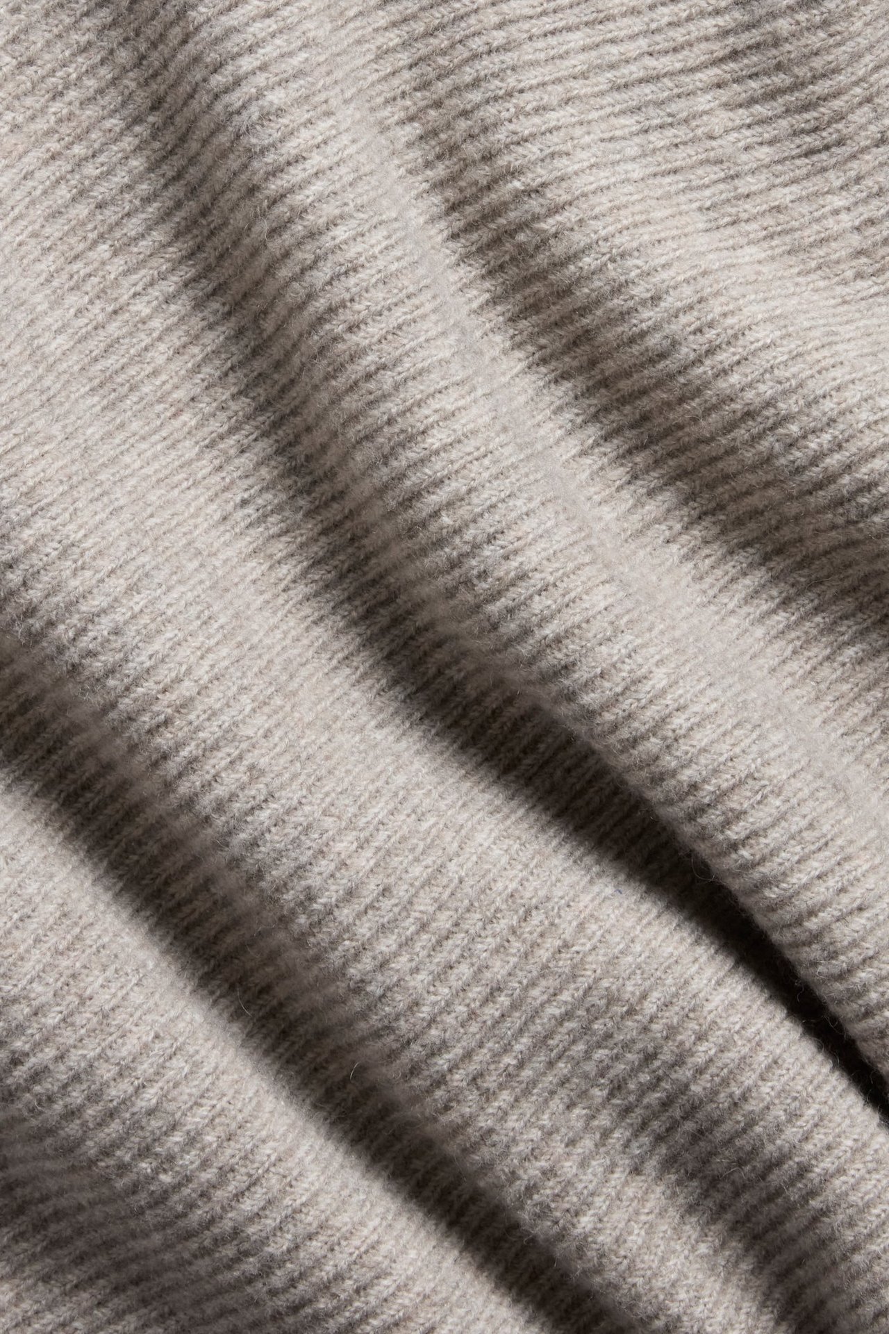 Zbliżenie beżowej melanżowej dzianiny z subtelną prążkowaną fakturą.