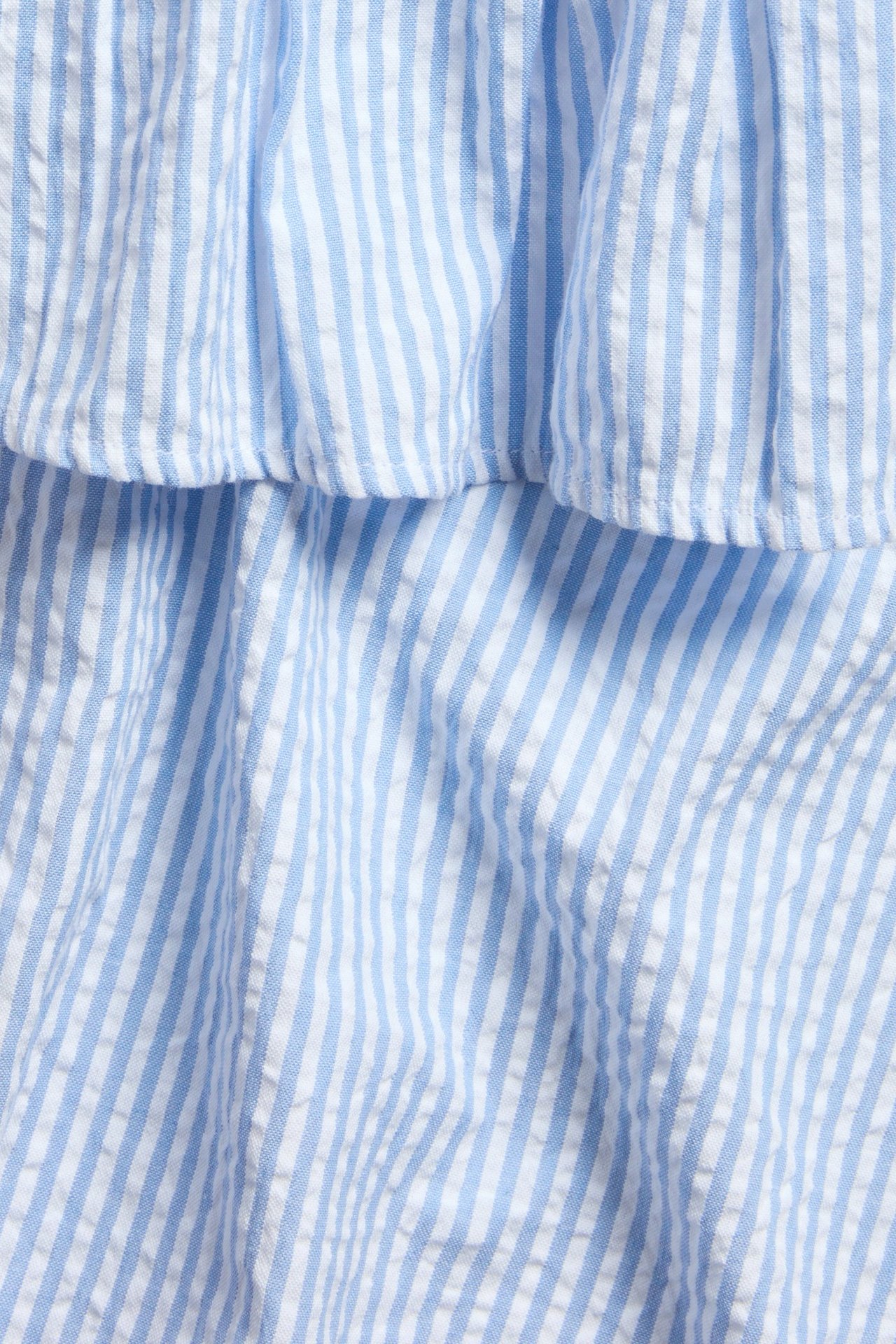 Zbliżenie na niebiesko-białą bawełnianą tkaninę w paski z falbaną topu.