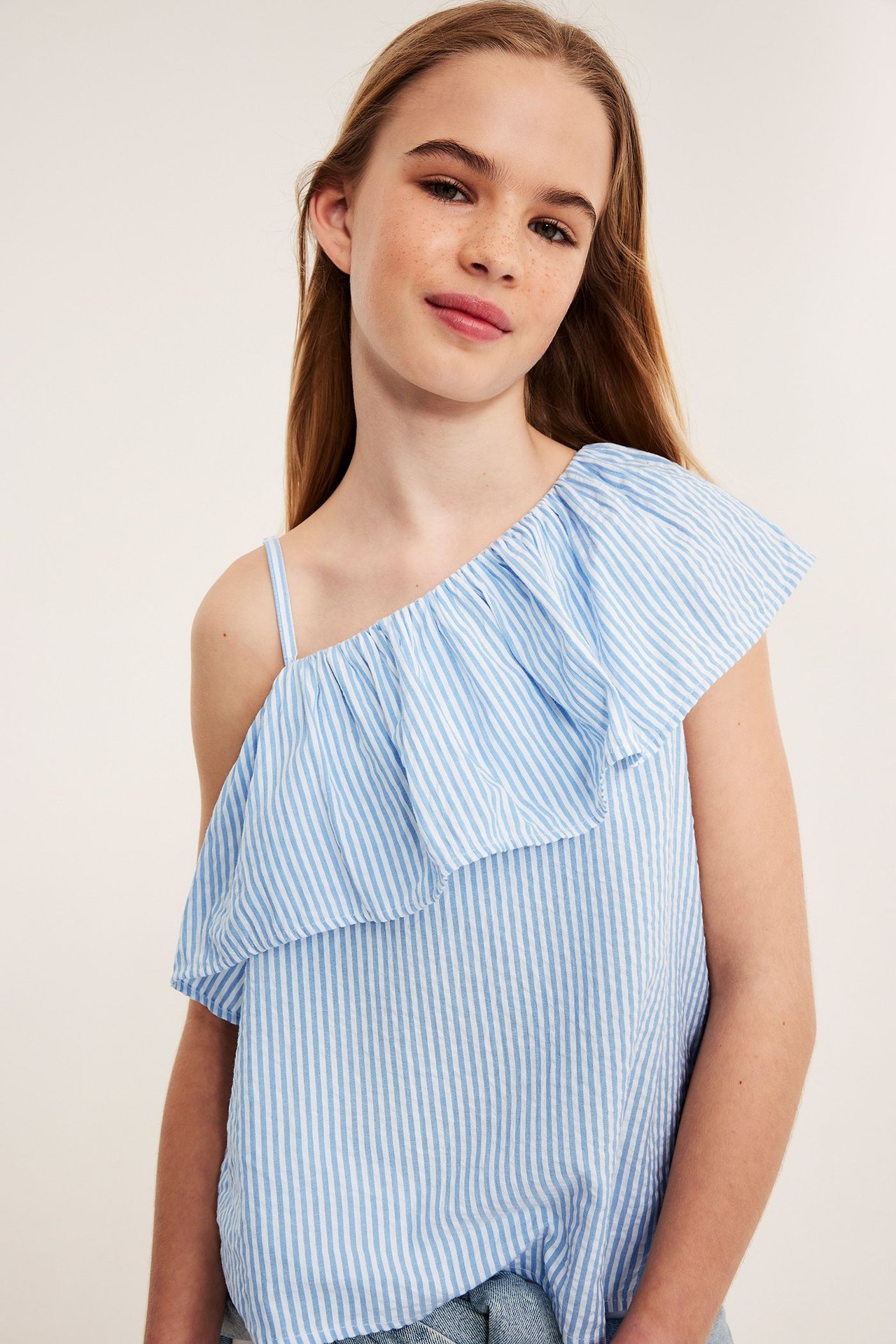 Lähikuva edestä: lapsi yksiolkaimisessa sinivalkoraidallisessa puuvillatopissa, jossa on röyhelö.