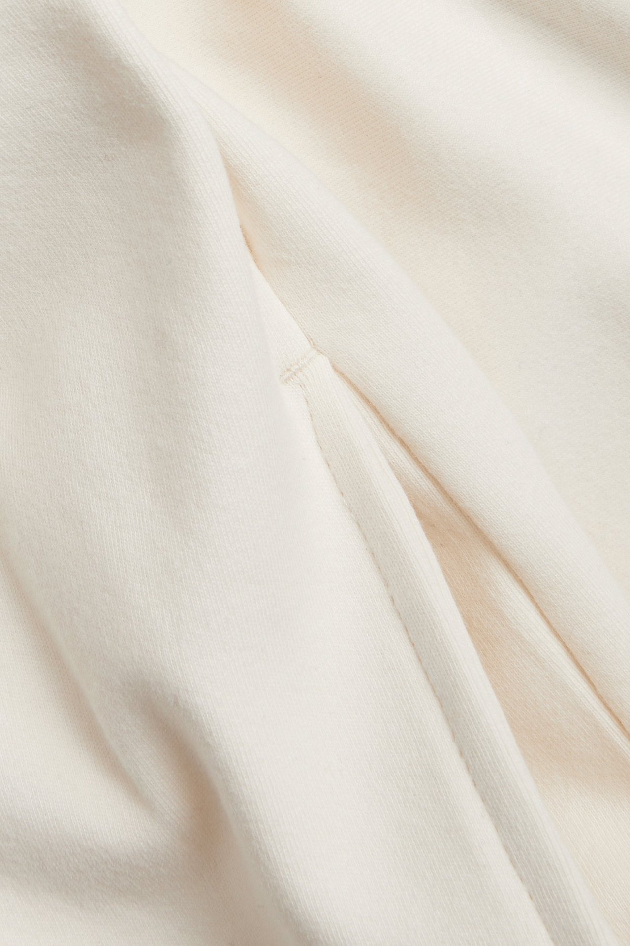 Närbild av en offwhite jerseyklänning, som visar ett insnitt med tygveck.