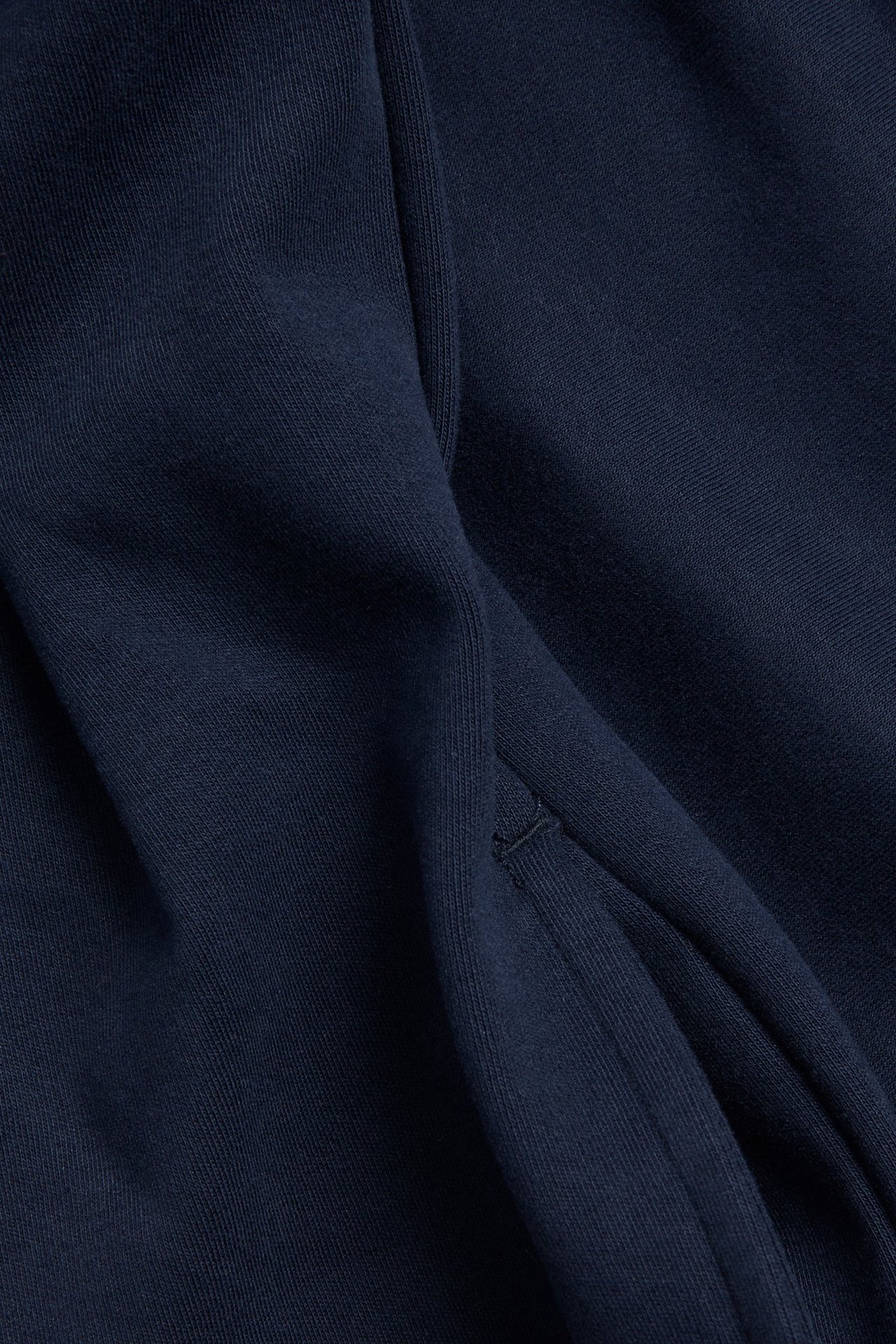 Närbild på mörkblått jerseyklänningstyg med sydda veckdetaljer.