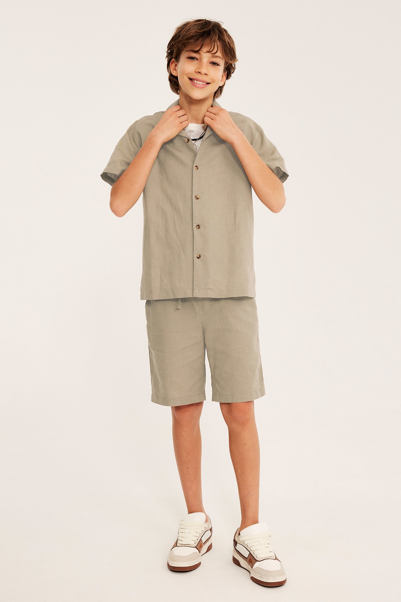 Framifrån: Barn i beiga linneshorts, matchande kortärmad skjorta över vit t-shirt och sneakers.