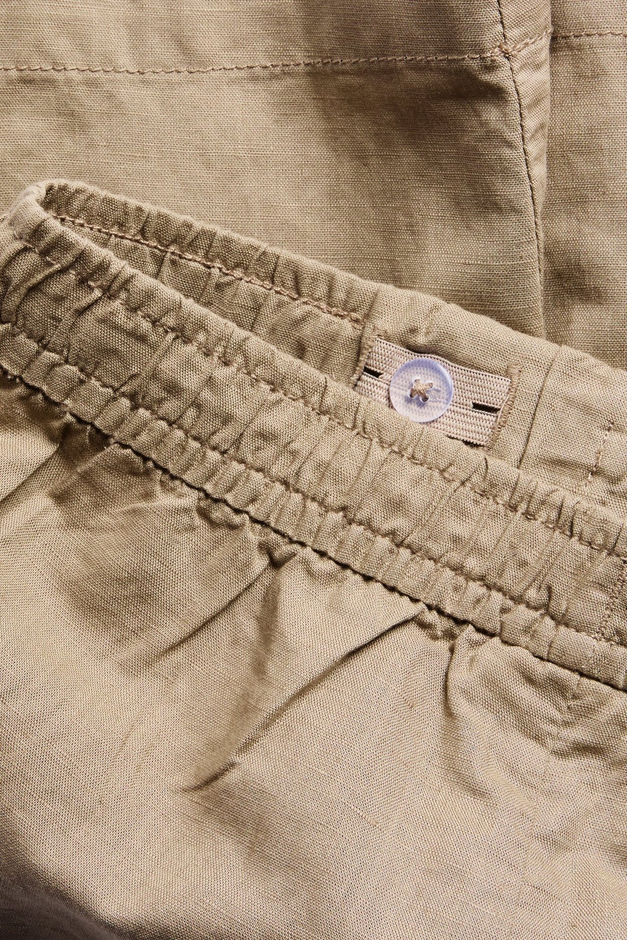 Lähikuva beigestä pellavasekoiteshortsista, jossa näkyy joustava säädettävä vyötärönauha napilla.