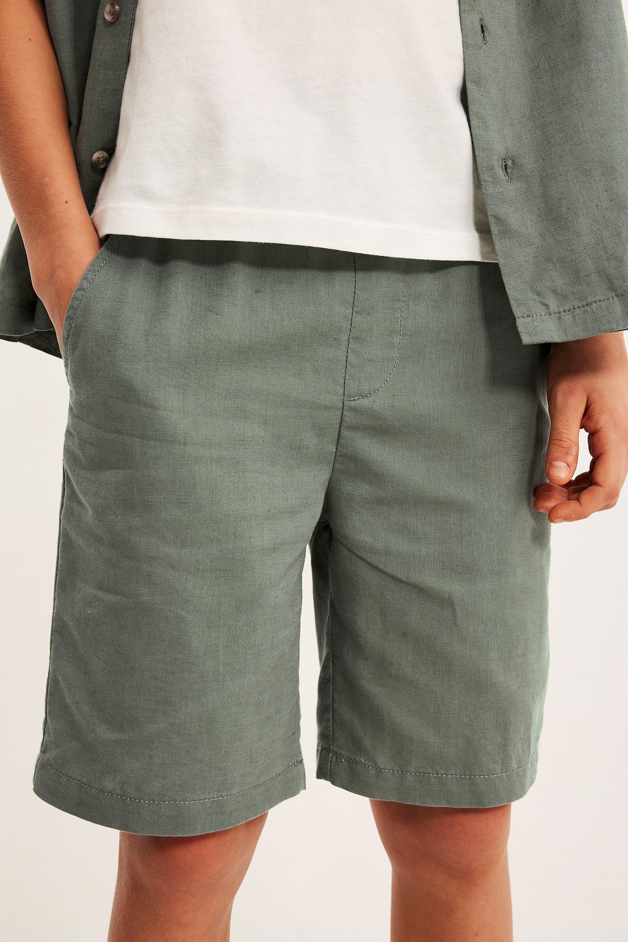 Lähikuva: lapsi vihreissä pellavashortseissa, valkoisessa t-paidassa ja avoimessa vihreässä paidassa.