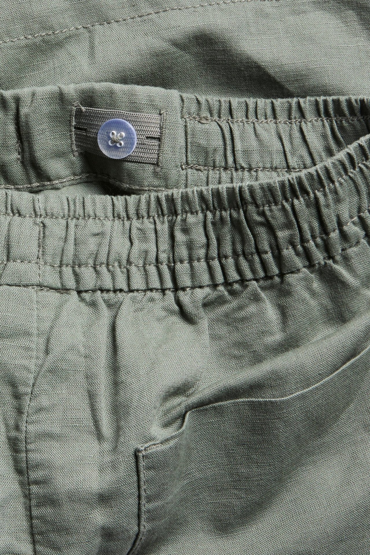 Lähikuva vihreistä pellavasekoiteshortseista, joissa on joustava vyötärö, säädettävä nappikuminauha ja näkyvä sivutasku.