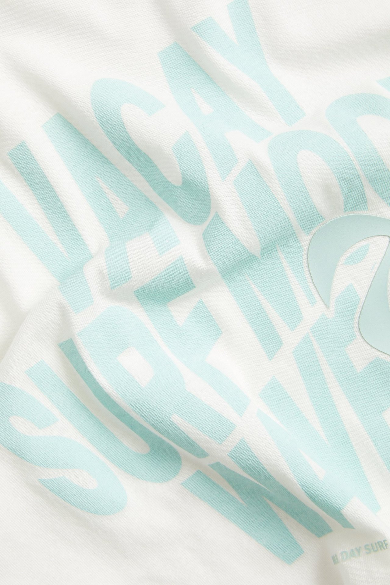 Lähikuva luonnonvalkoisesta puuvillaisesta oversize-lasten t-paidasta, jossa vaaleansininen graafinen etupainatus.