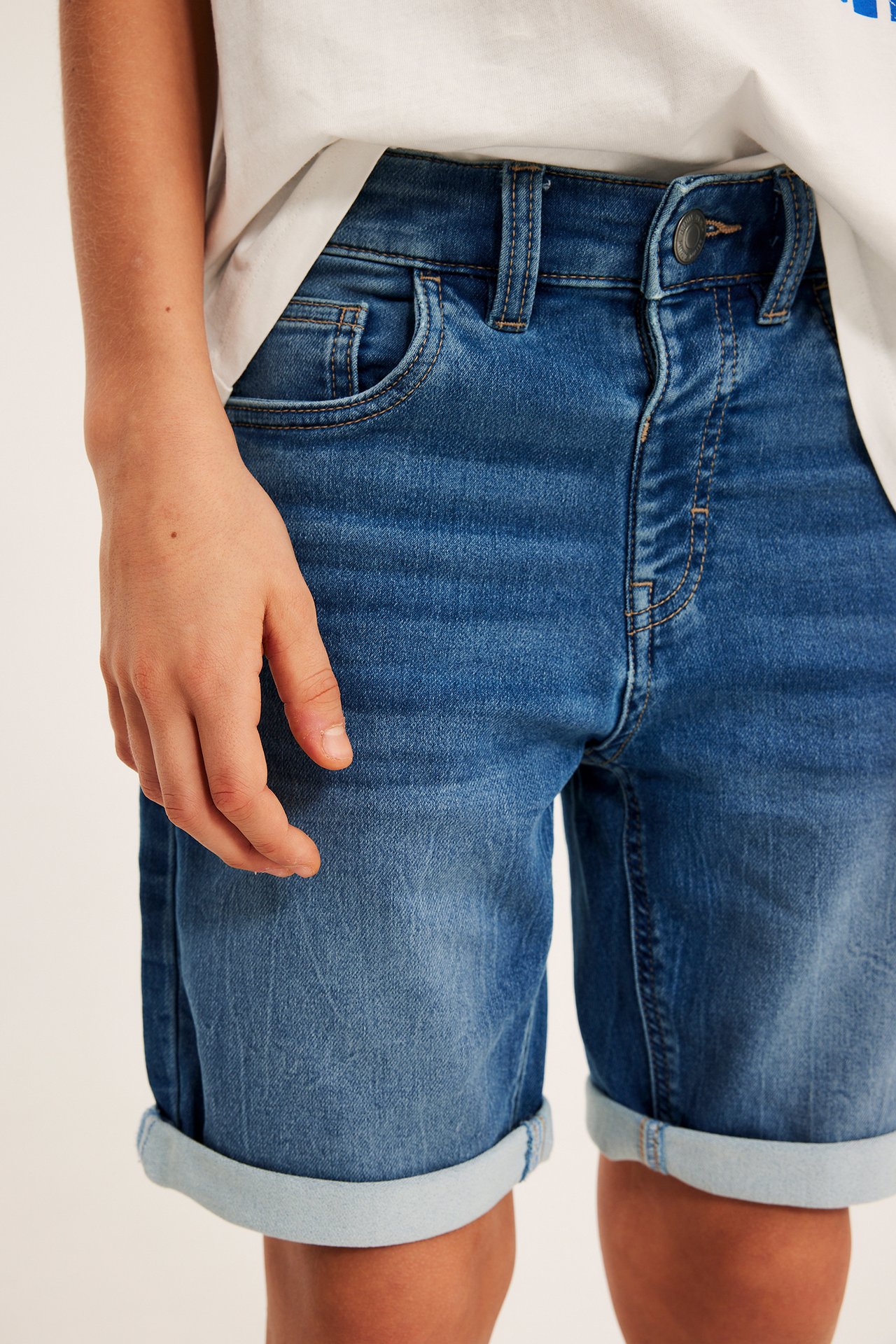 Närbild framifrån av barn i ljusblå stretchiga jeansshorts med uppvikta benslut och vit t-shirt.