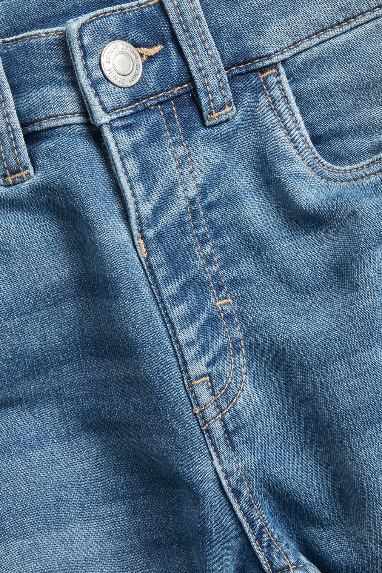 Zbliżenie na jasnoniebieskie dżersejowe szorty jeansowe z metalowym guzikiem i widocznymi szwami.