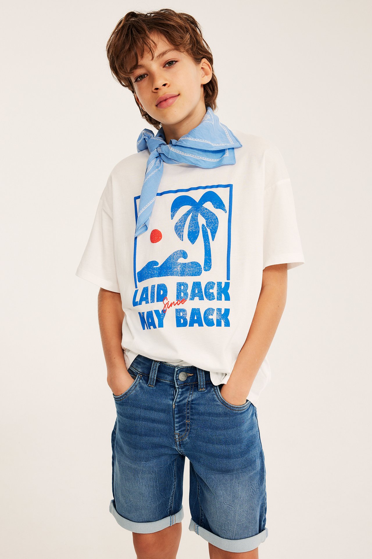 Dziecko w jasnoniebieskich elastycznych szortach jeansowych, białej koszulce i jasnoniebieskiej bandanie.