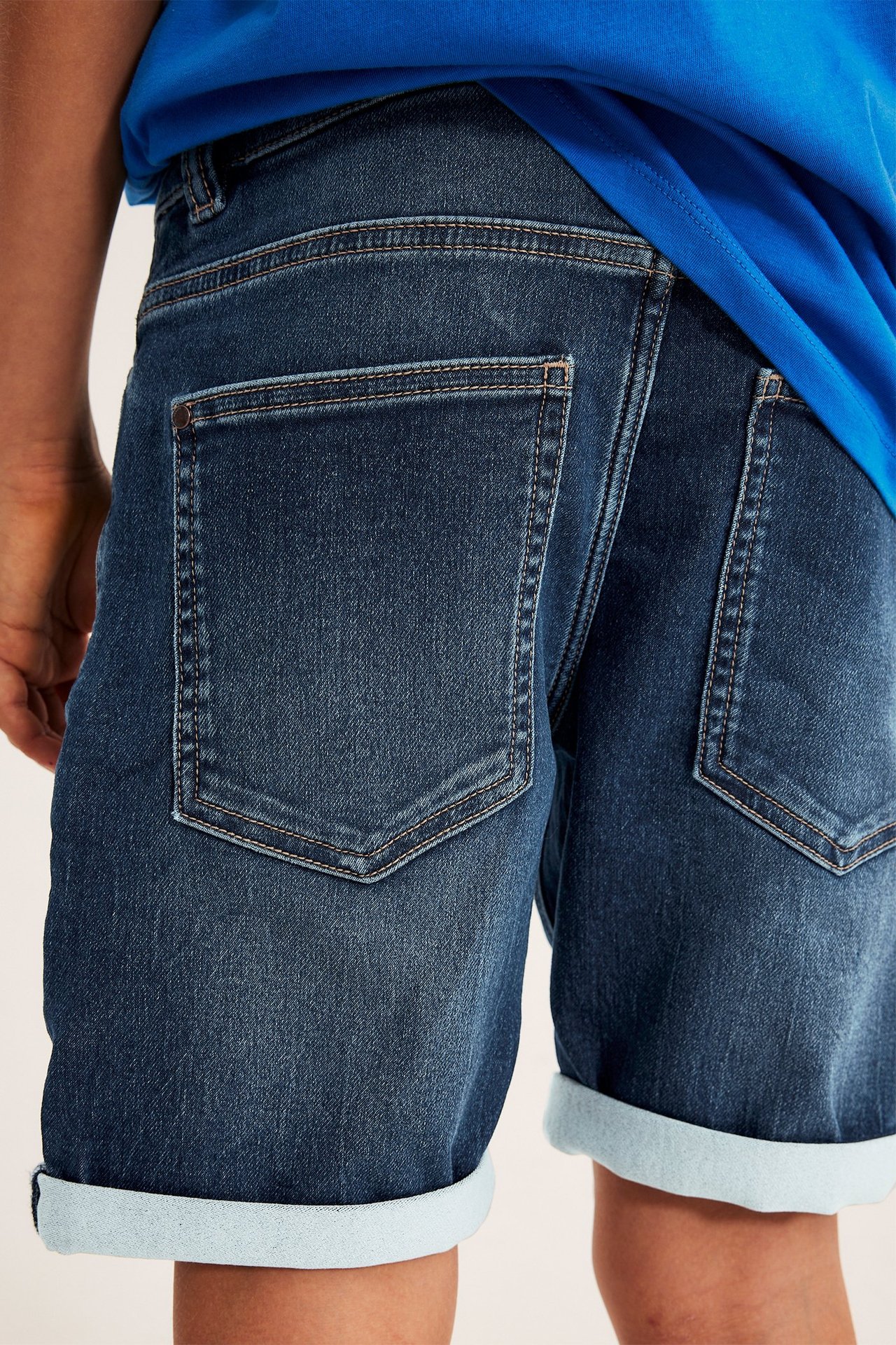 Bakifrån på barn i mörkblå stretchiga jeansshorts med uppvikta muddar och blå t-shirt.