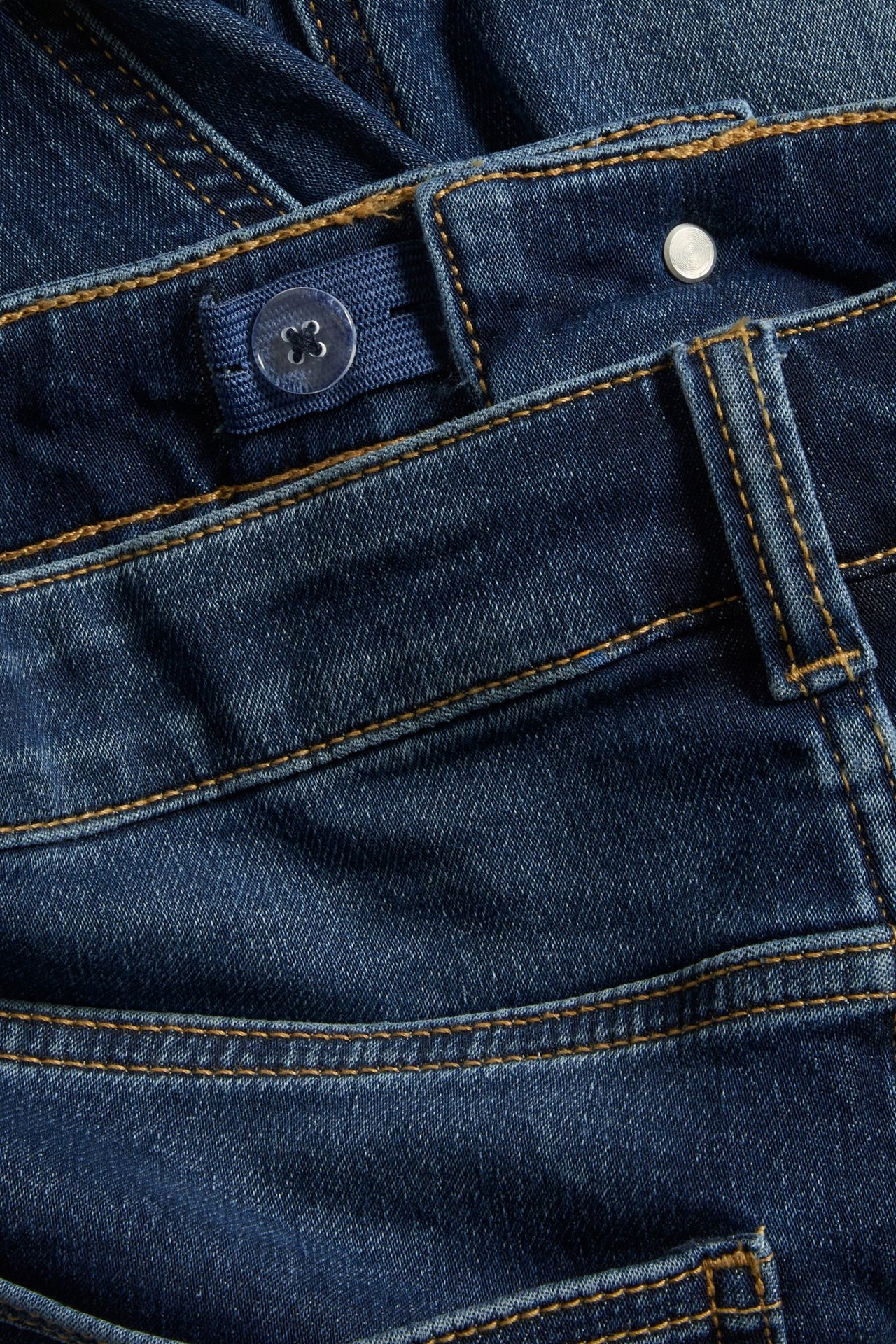 Zbliżenie granatowych szortów dżinsowych z dżerseju, z regulowaną elastyczną talią i kontrastowymi przeszyciami.