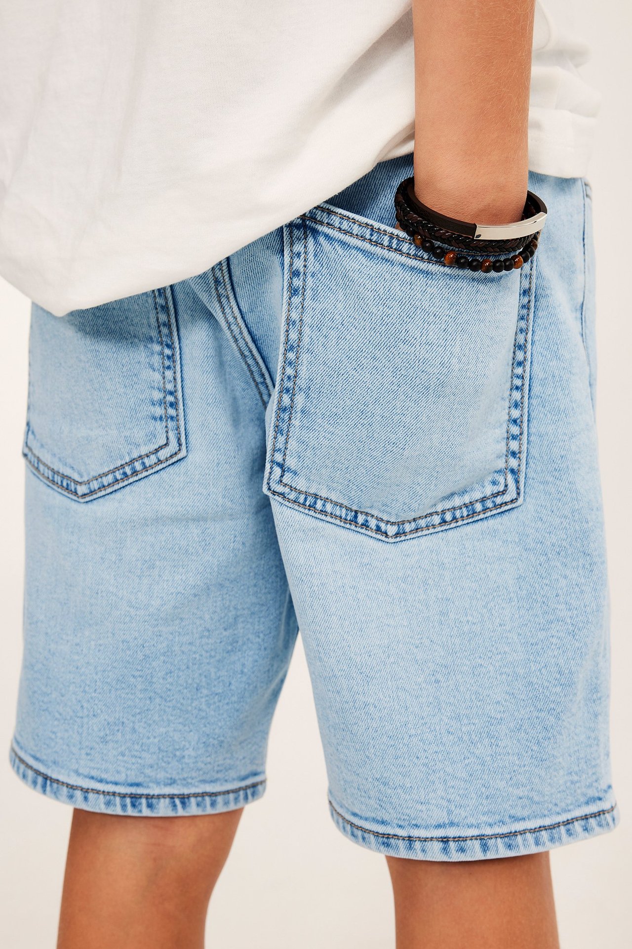 Zbliżenie dziecka w jasnoniebieskich szortach jeansowych, białej koszulce i koralikowych bransoletkach.